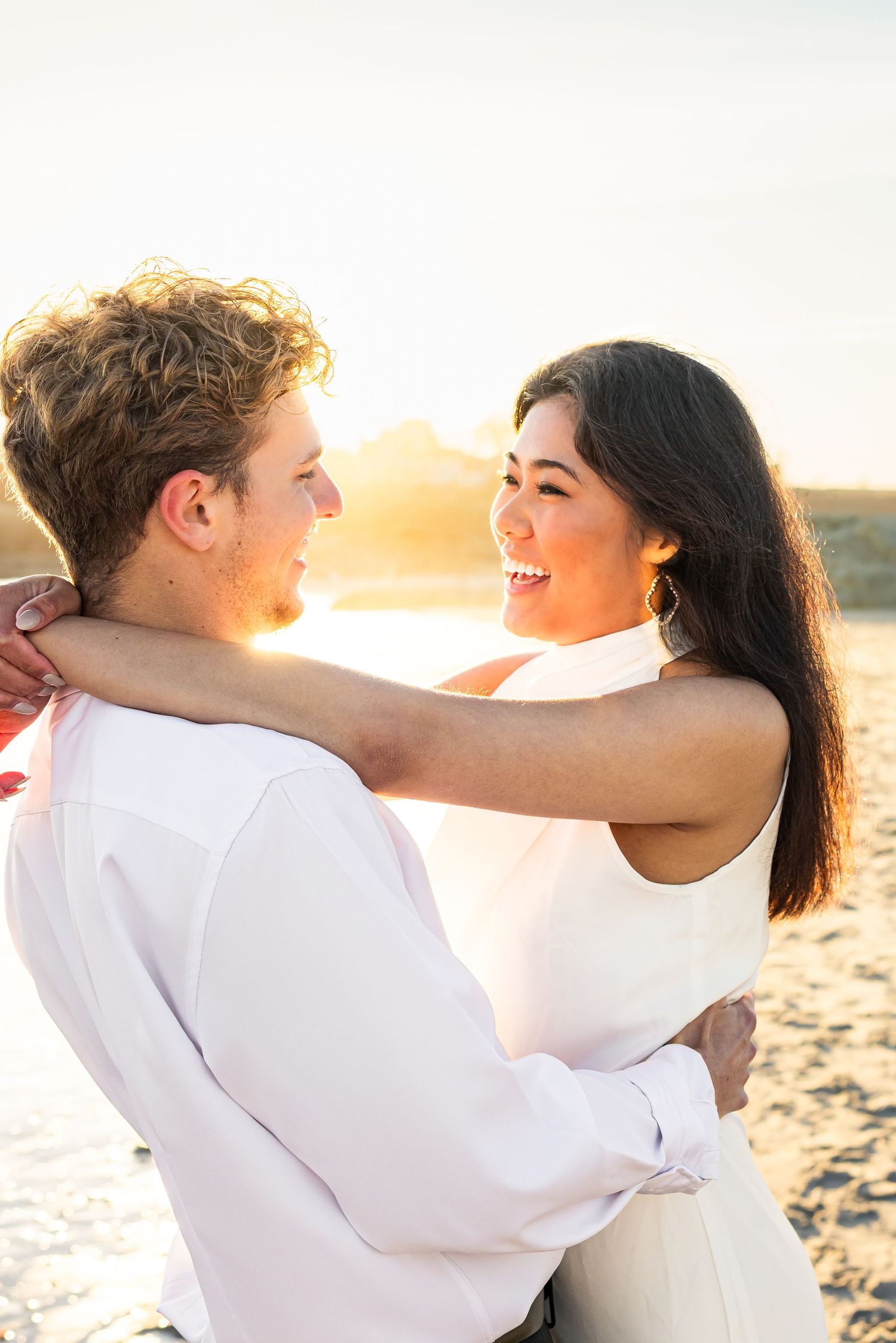 Happy couple embracing and smiling at each other on beach during beautiful golden sunset.