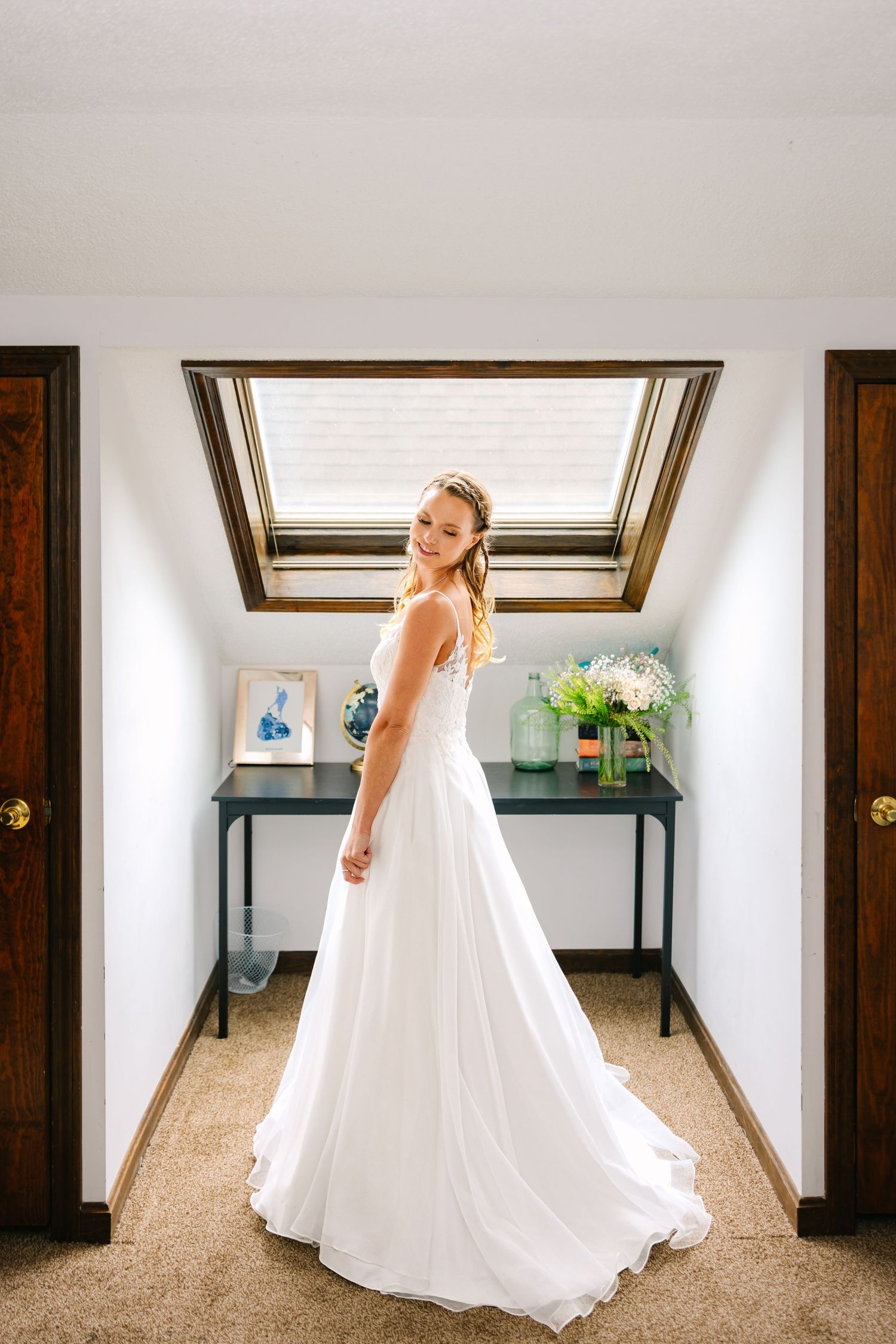 A bride wearing a long wedding dress poses by a sunlit window with decorative archway at intimate wedding getting ready in Connecticut