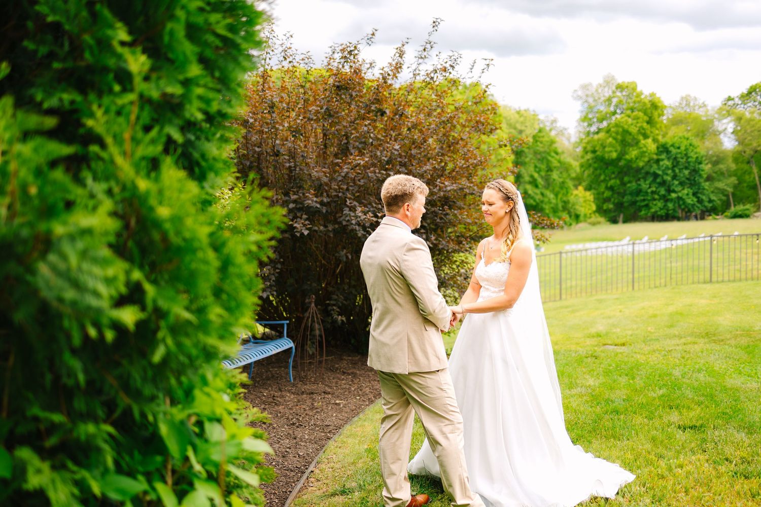A couple in formal wedding attire shares a romantic dance in a lush green garden setting.