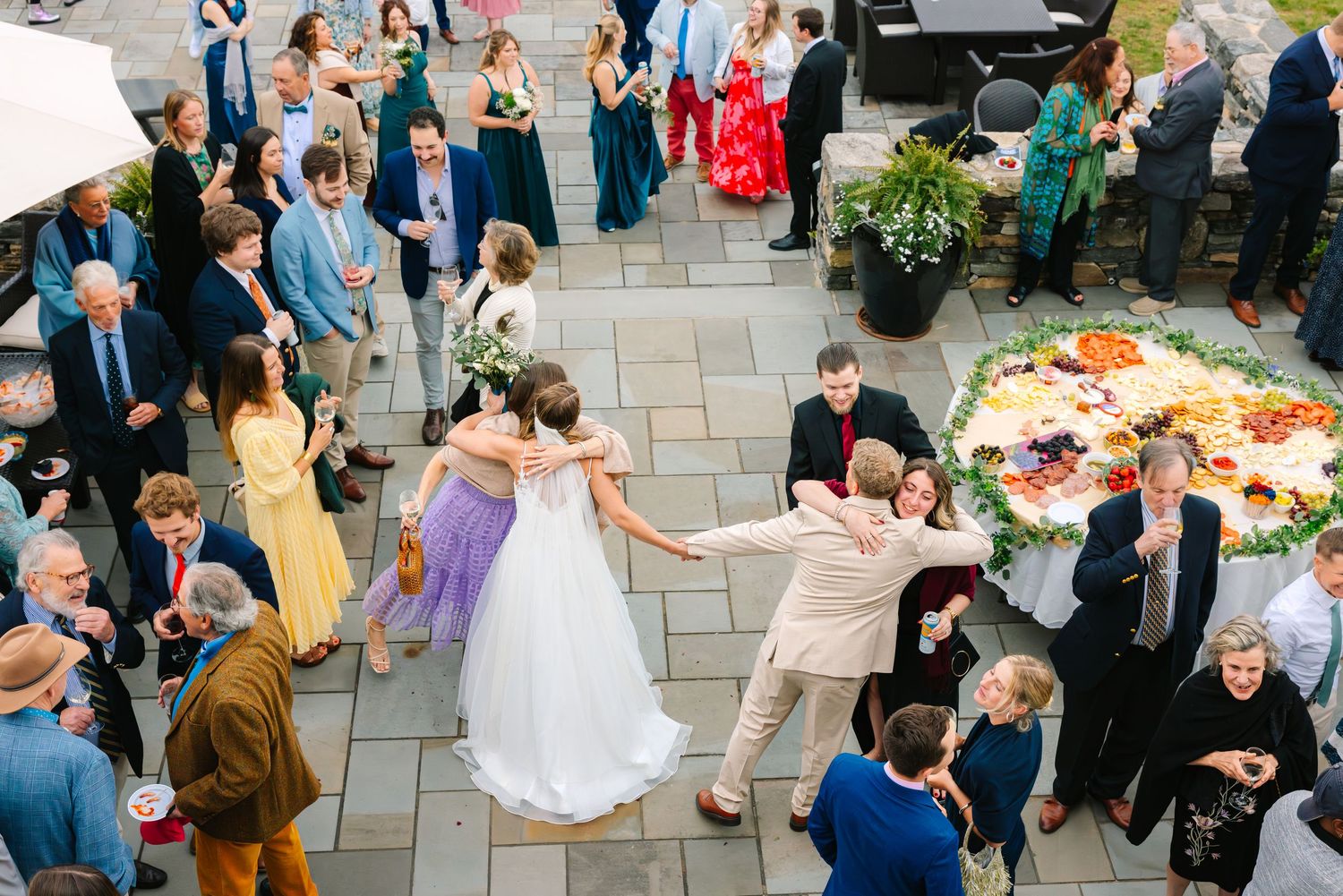 Wedding guests gather around a colorful buffet spread on an outdoor patio during a festive celebration.