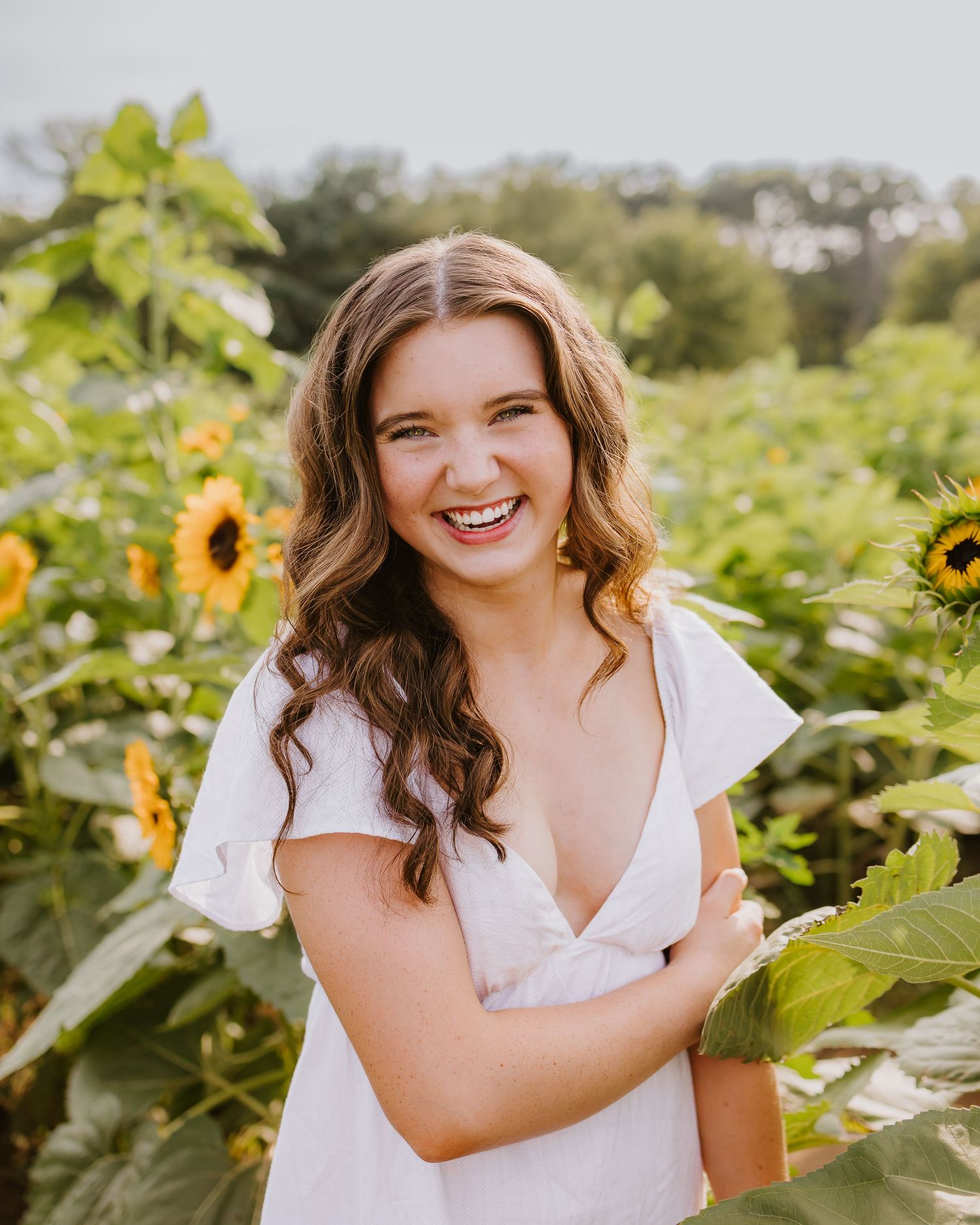 Young woman in white dress laughing joyfully in a vibrant sunflower field outdoors.