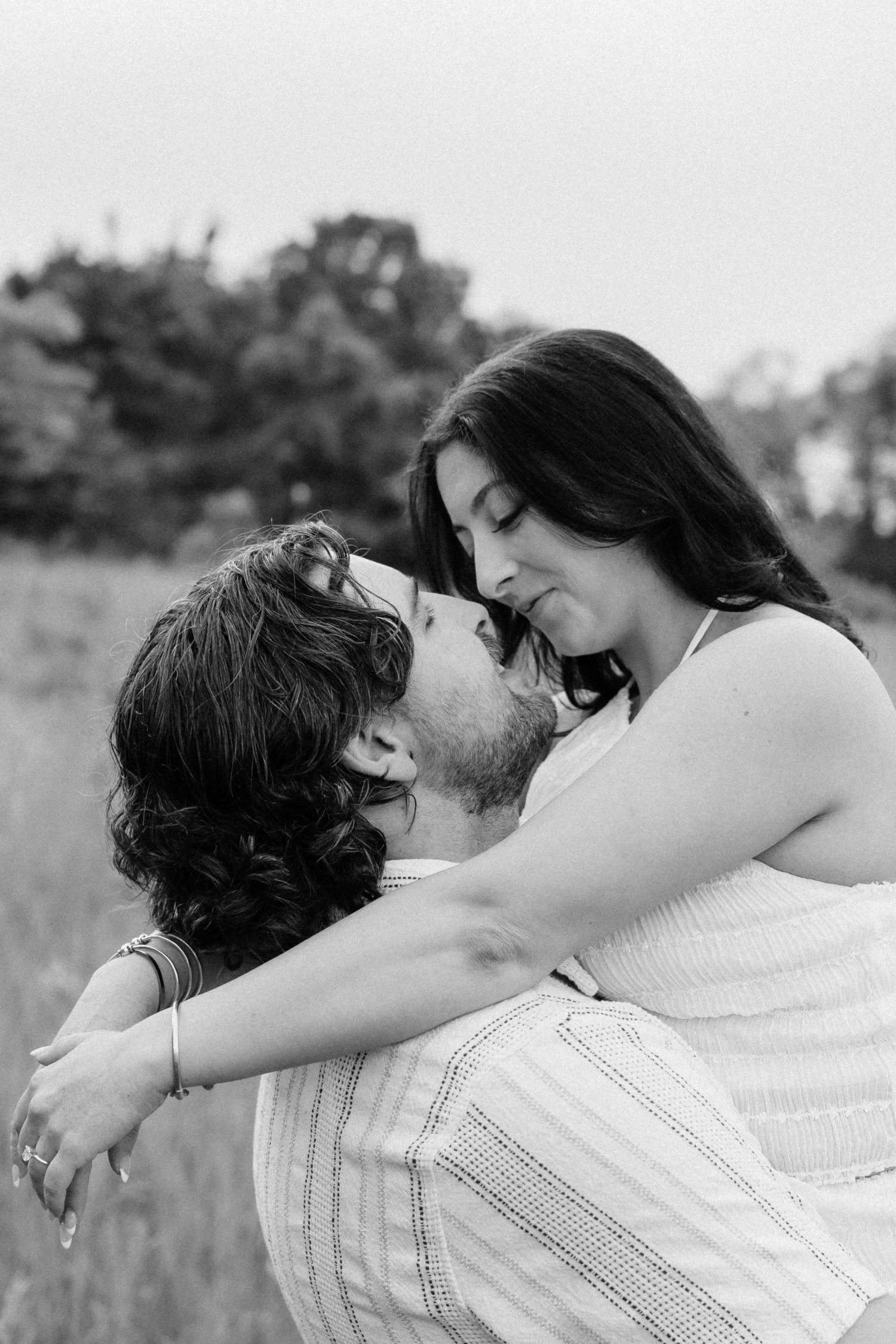 Black and white photo of a man lifting a woman as they share a romantic kiss outdoors.