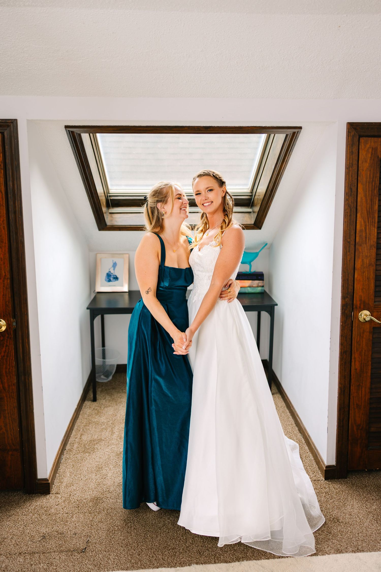 A bride in a white gown and her bridesmaid in navy blue share a joyful moment before the wedding ceremony.