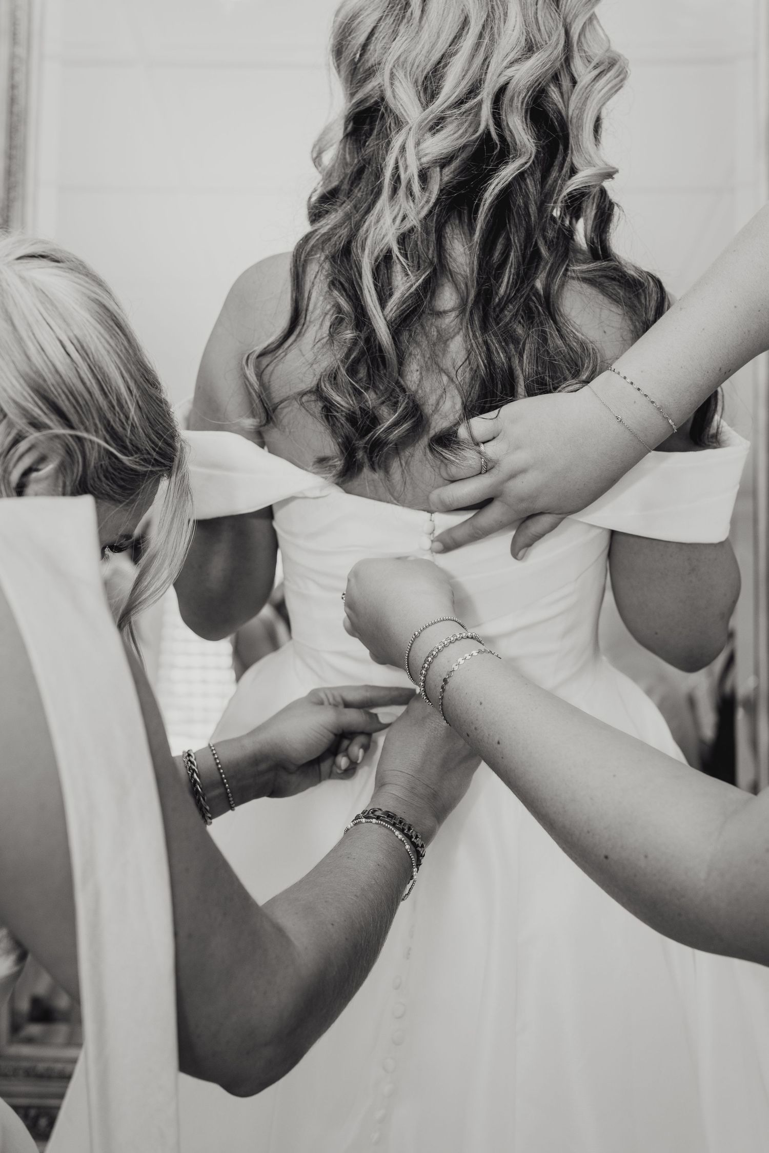 Black and white photo of bride being helped into a white wedding dress by bridesmaids at The Regatta Place in Newport Rhode Island