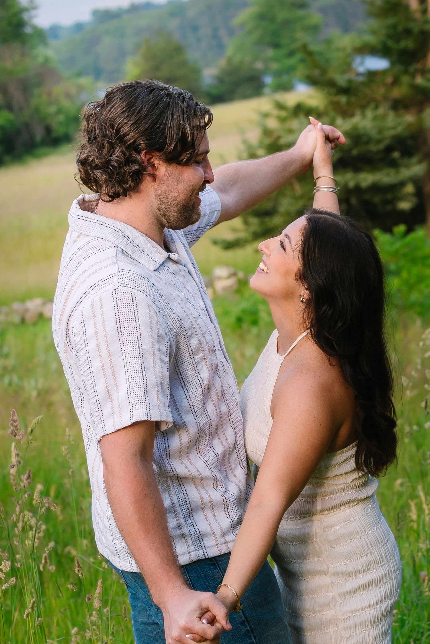 Couple laughing and holding hands as man twirls woman in a green summer meadow.