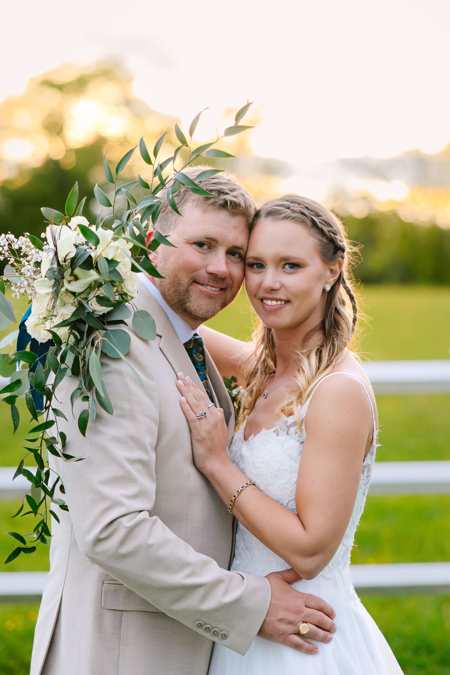 A romantic sunset wedding photoshoot in an open field with green foliage decorations and soft golden lighting.