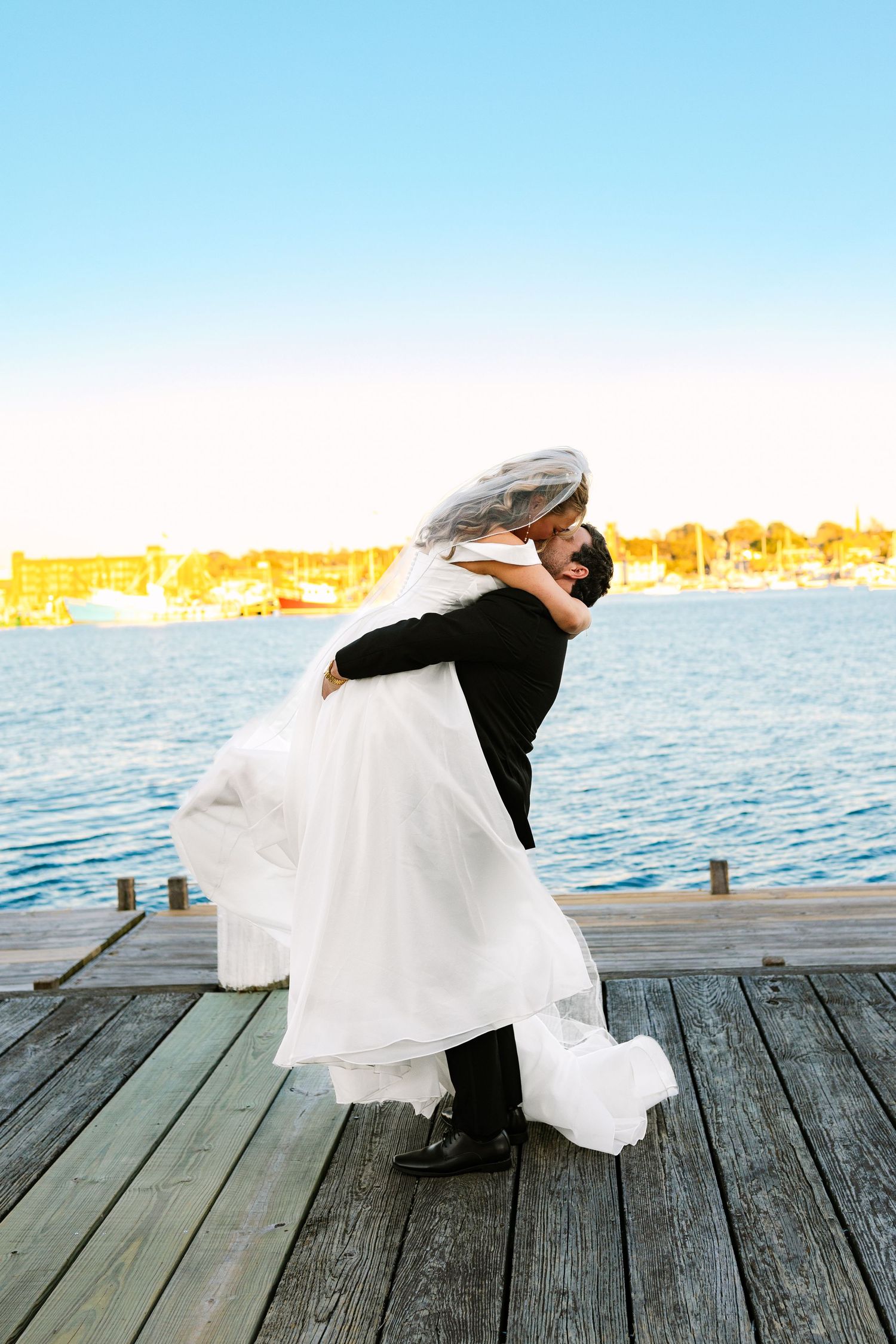 A bride and groom twirl and dance joyfully on a boat dock at sunset golden hour at The Regatta Place in Newport Rhode Island