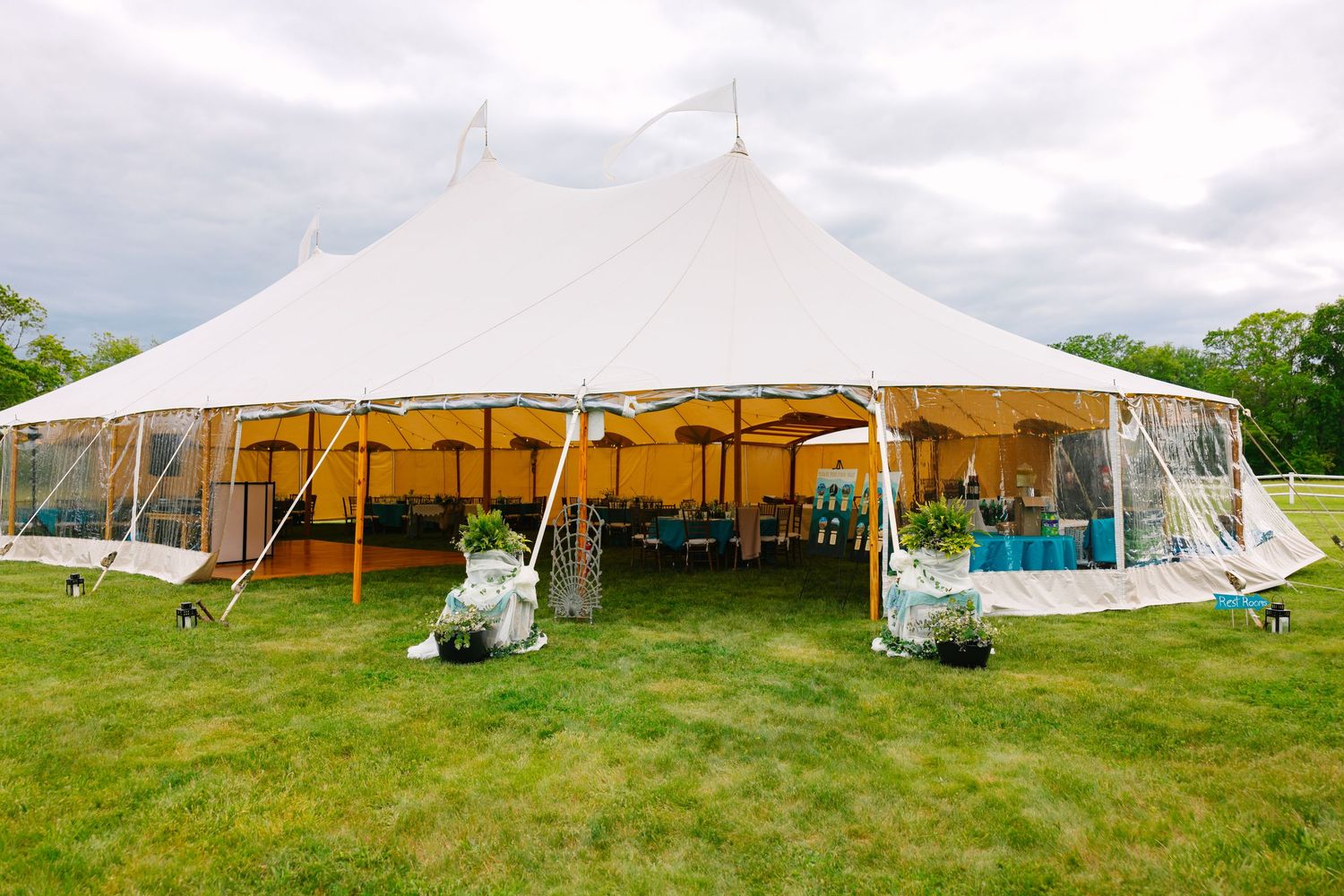 Multiple large white stretch tents set up in green fields for outdoor events against blue sky background.