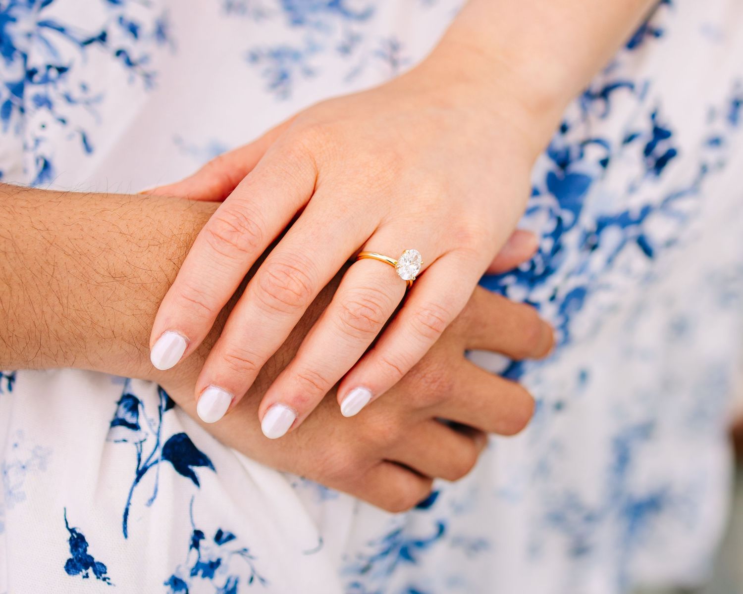 Close-up of hands showing a gold solitaire diamond engagement ring on a woman's finger, wearing a blue floral dress in Newport Rhode Island