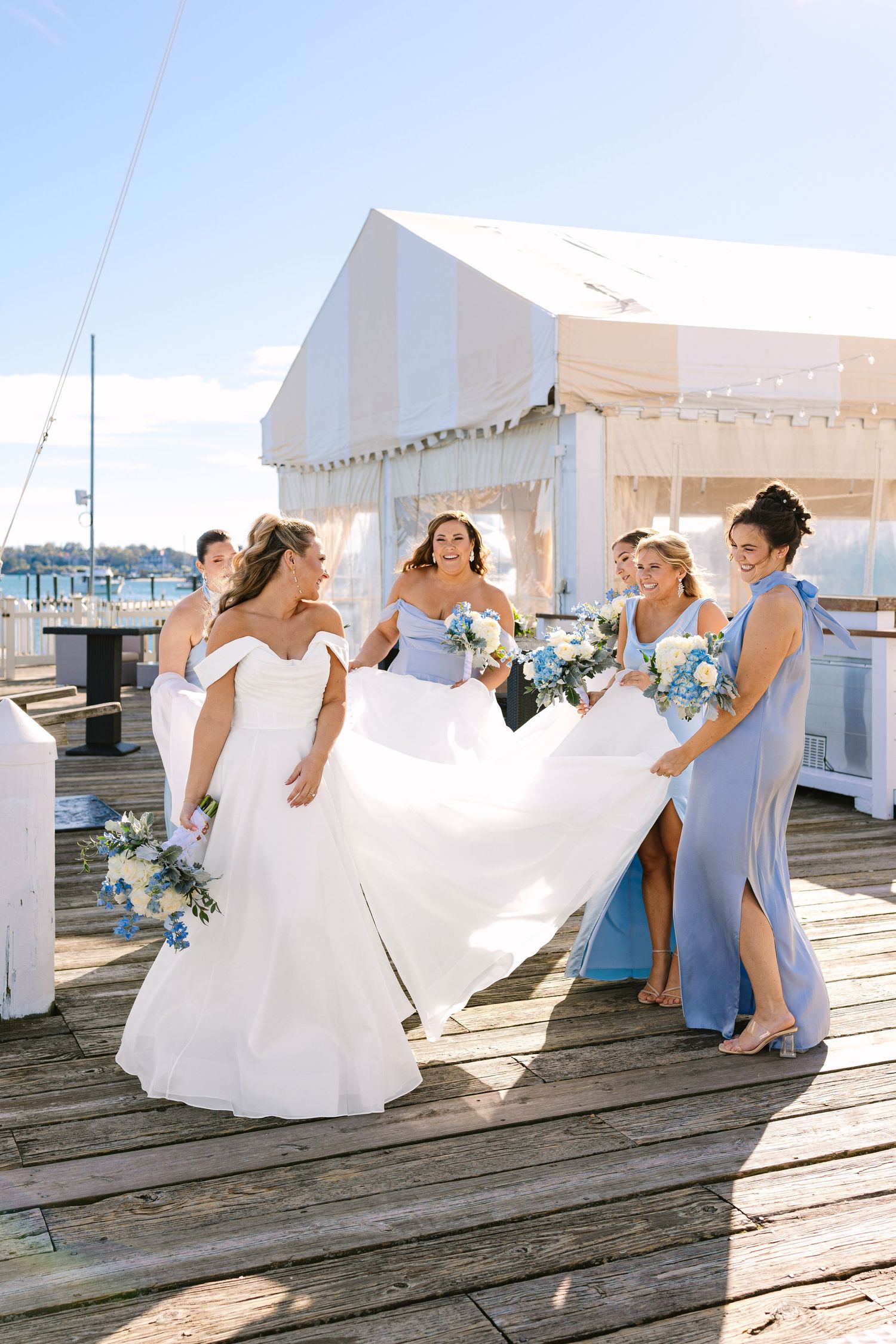 Bride with her bridal party naturally fixing her dress outside of the wedding venue The Regatta Place in Newport, Rhode Island