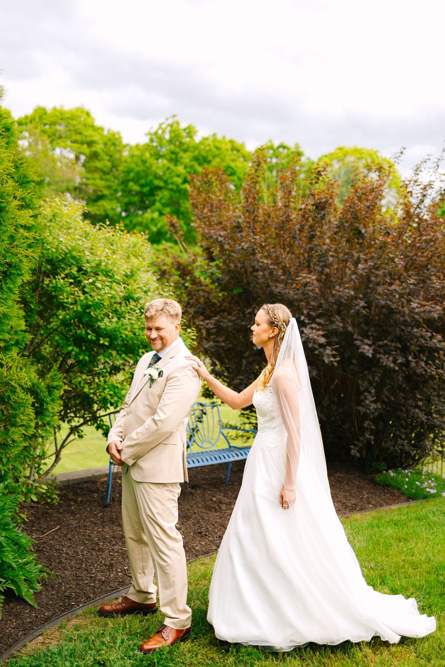 Wedding couple shares a fun first look moment in a lush garden setting with beautiful landscaping and greenery.