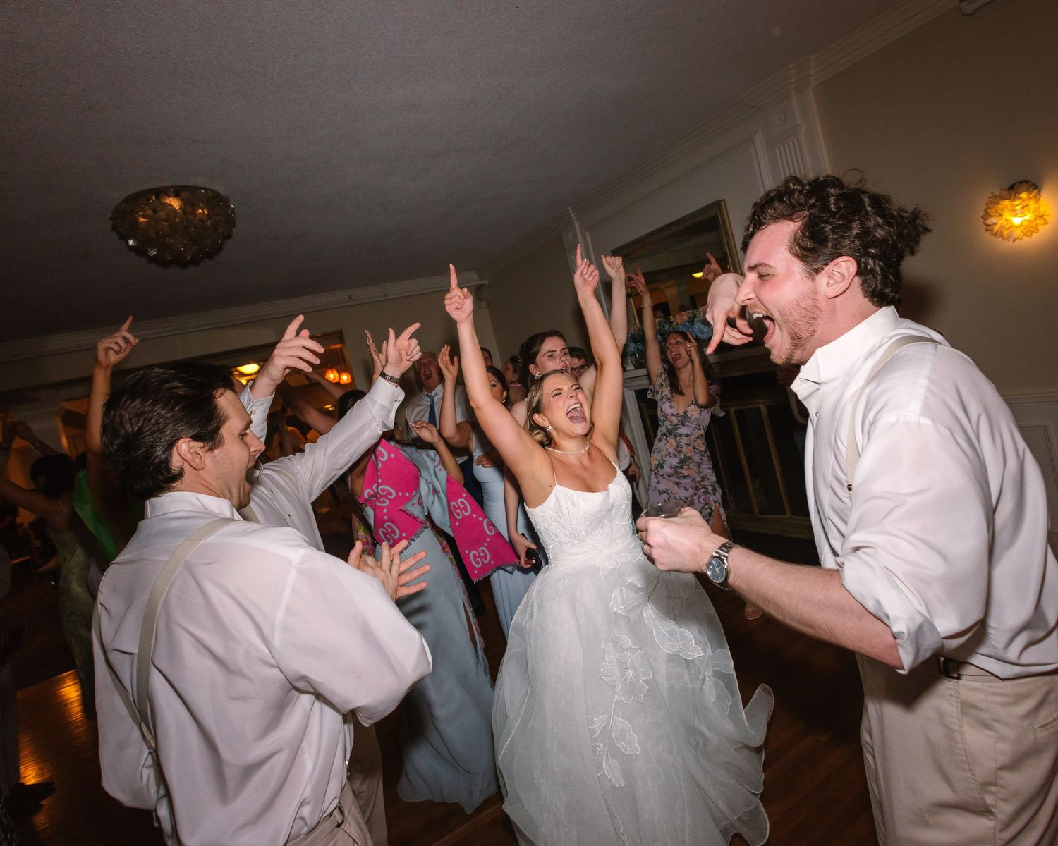Joyful bride in white gown celebrates with guests on a lively wedding reception dance floor.