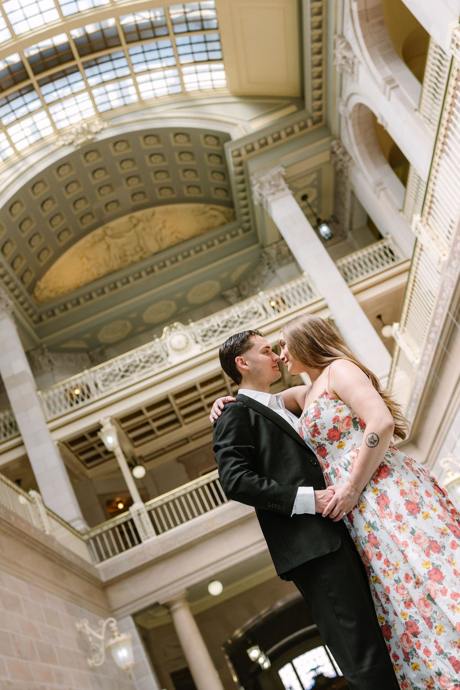 Couple sharing a kiss beneath an ornate domed ceiling with classical columns in a historic building.