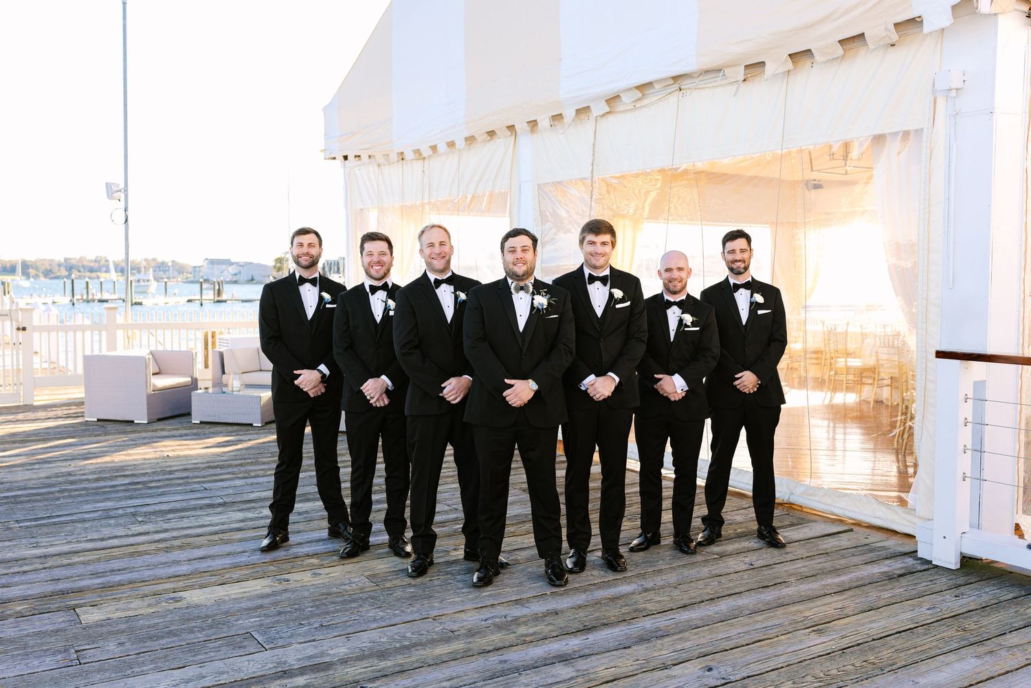 Groomsmen in black tuxedos pose together on white steps for formal wedding photos at The Regatta Place in Newport Rhode Island