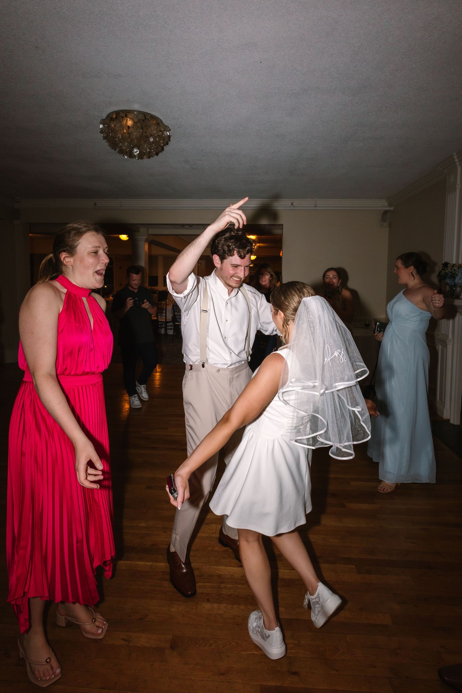 Bride in white dress and veil dances energetically with groom and guests at wedding reception at Warwick Country Club in Rhode Island.