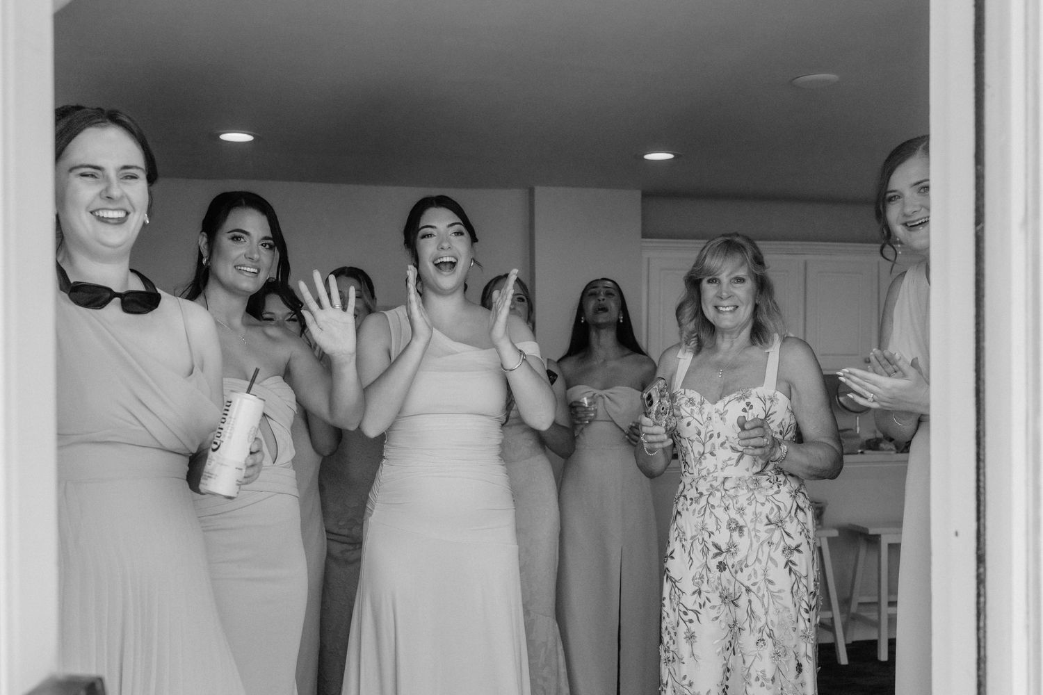 Excited bridesmaids in neutral dresses celebrating together in black and white wedding photo.