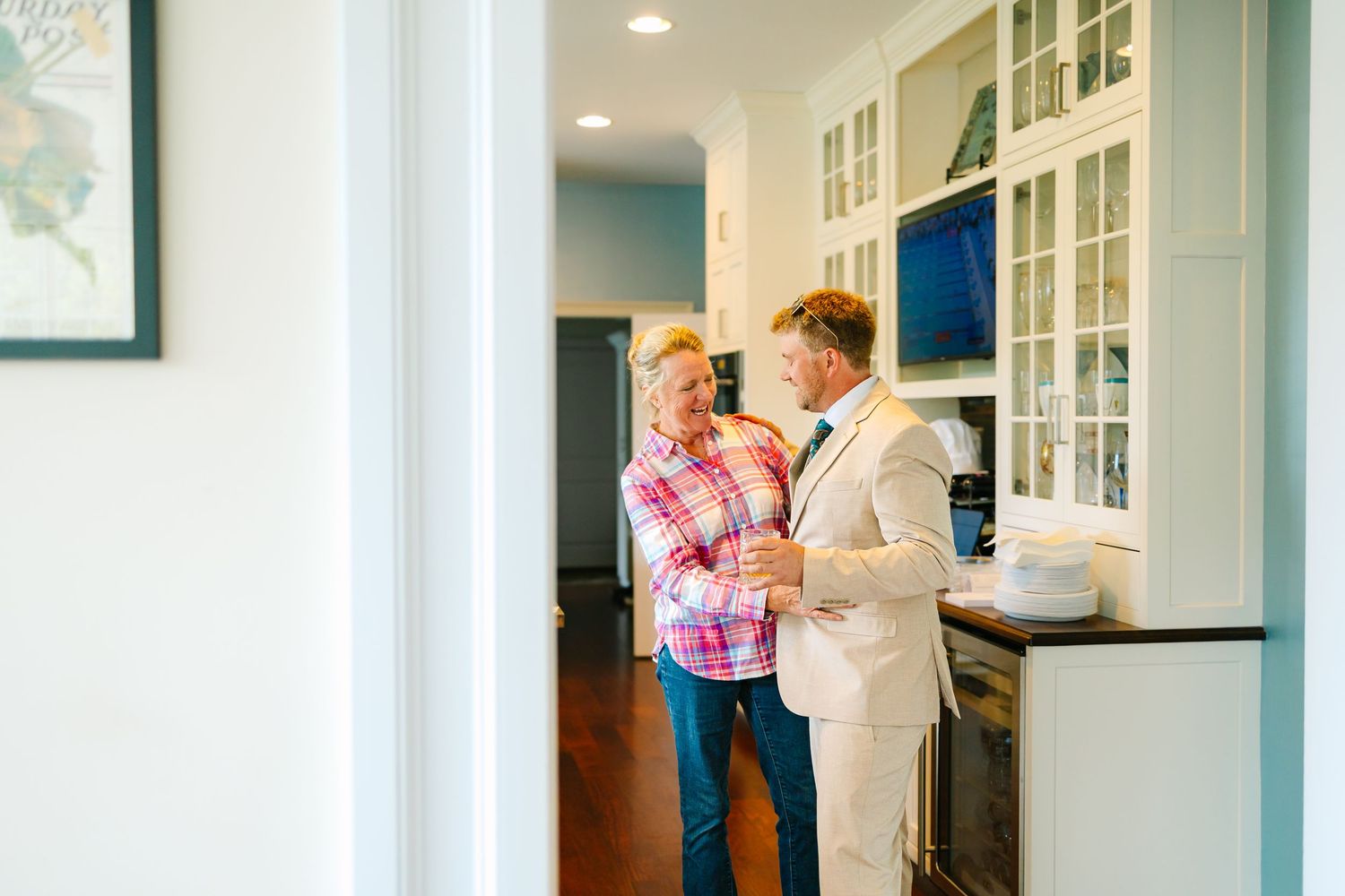 Mother and son share a tender moment while standing together in a bright modern kitchen with white cabinetry getting ready for wedding day
