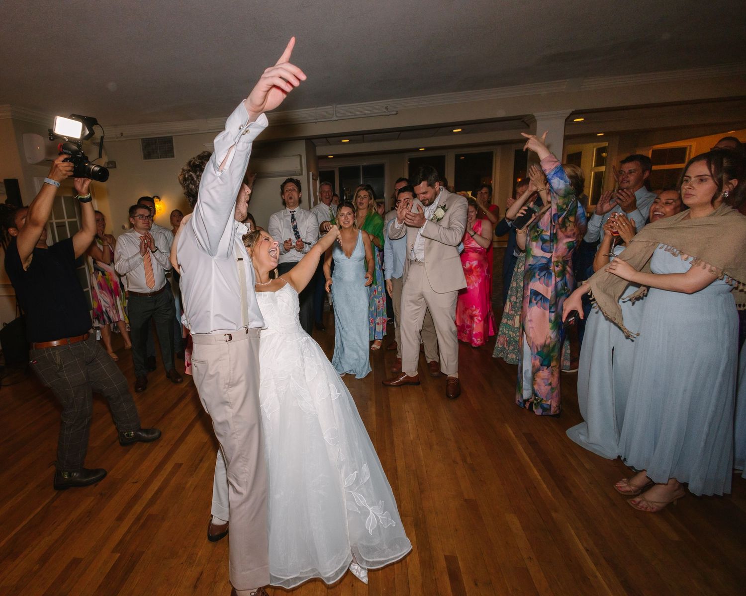 Groom pointing upward while dancing with bride surrounded by celebrating guests at wedding reception at Warwick Country Club in Rhode Island