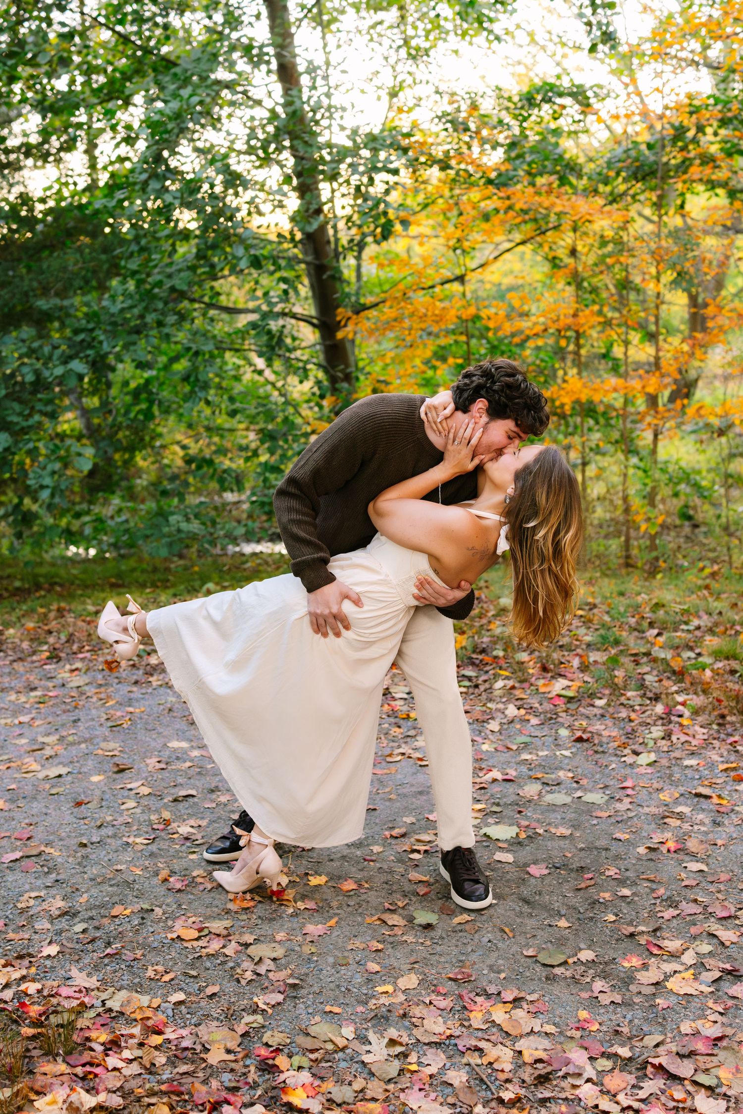 A romantic dip pose captured in autumn with colorful fallen leaves scattered on a forest path during sunset golden hour at Arnold Arboretum