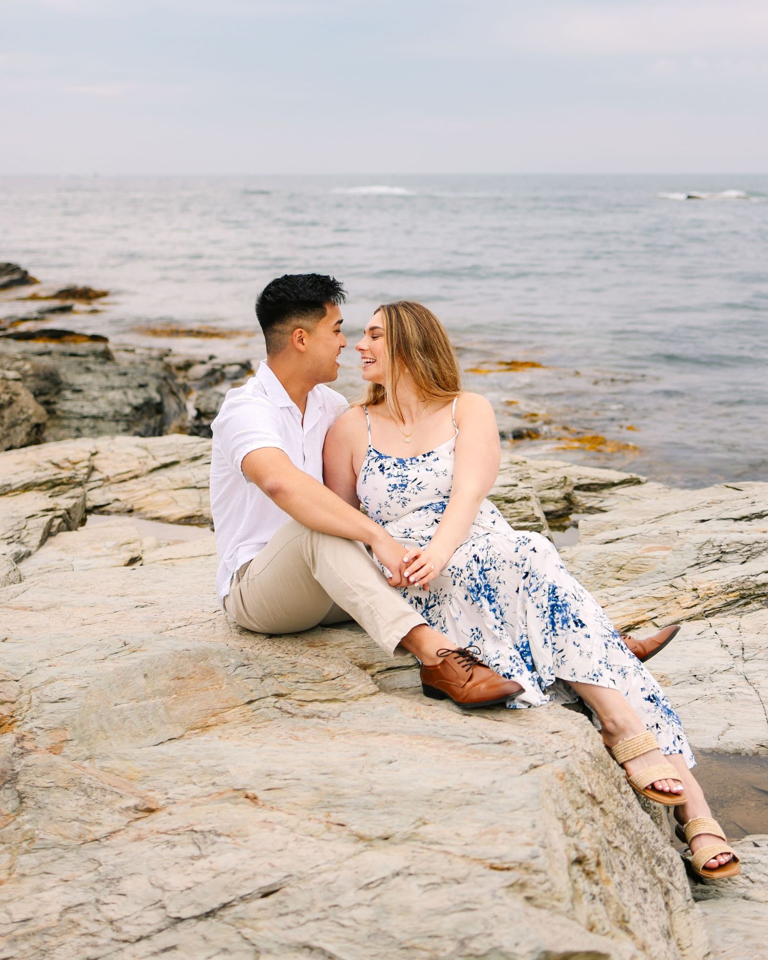 Couple sharing romantic moments on rocky coastal shoreline during sunset on Ocean Drive In Newport Rhode Island