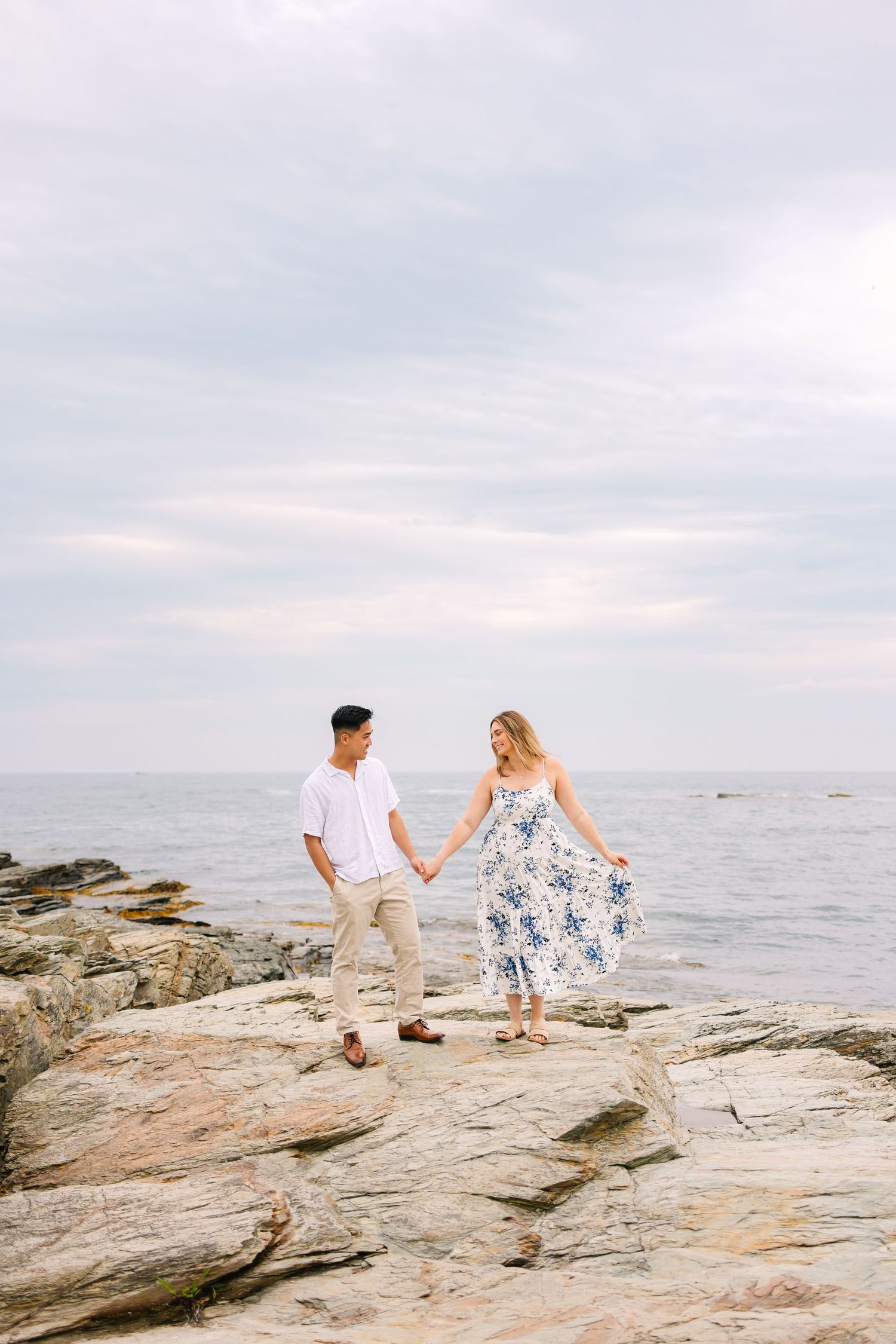 A newly engaged couple dance together during engagement photos on Ocean Drive in Newport Rhode Island on the rocky coastal oceanside cliffs