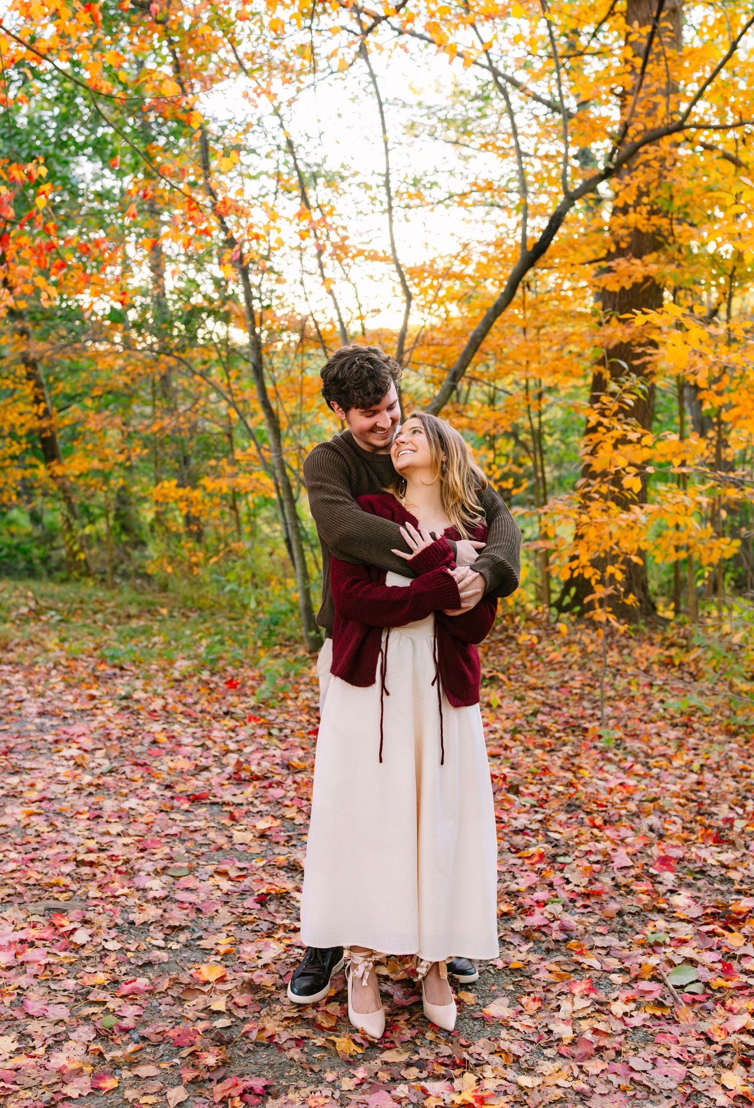 A romantic autumn scene with a couple embracing among vibrant orange foliage and fallen leaves on a forest path.