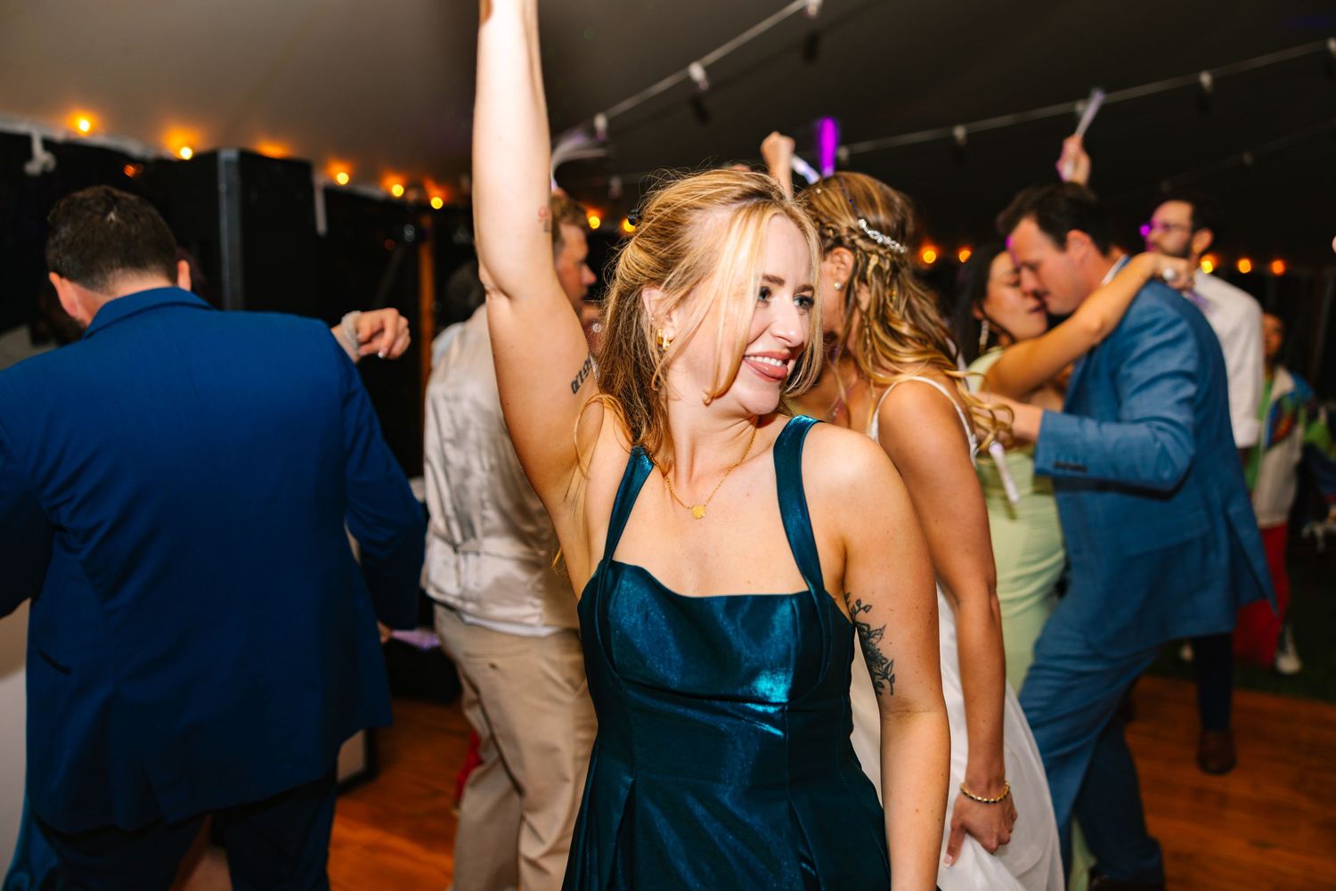 Wedding guests dance and celebrate together on a dimly lit dance floor at an evening reception.