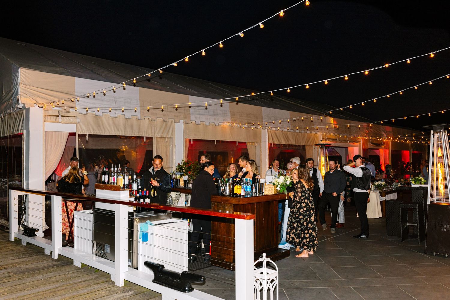 String lights illuminate a dark indoor event space with wooden beams and festive holiday decorations.