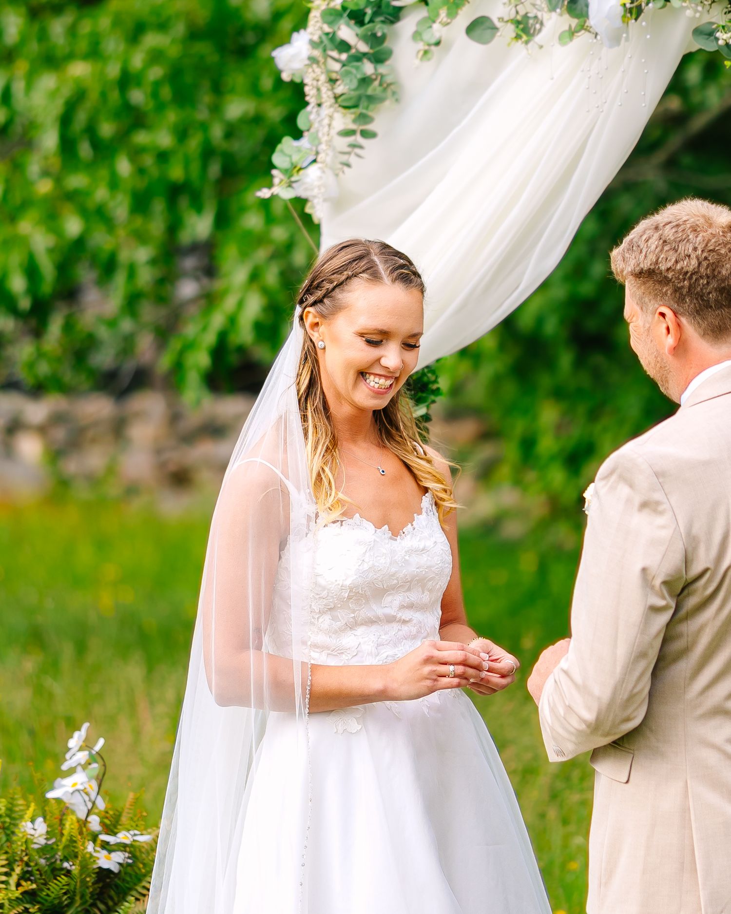 A couple shares a romantic moment during an outdoor wedding ceremony surrounded by lush greenery and white decor.
