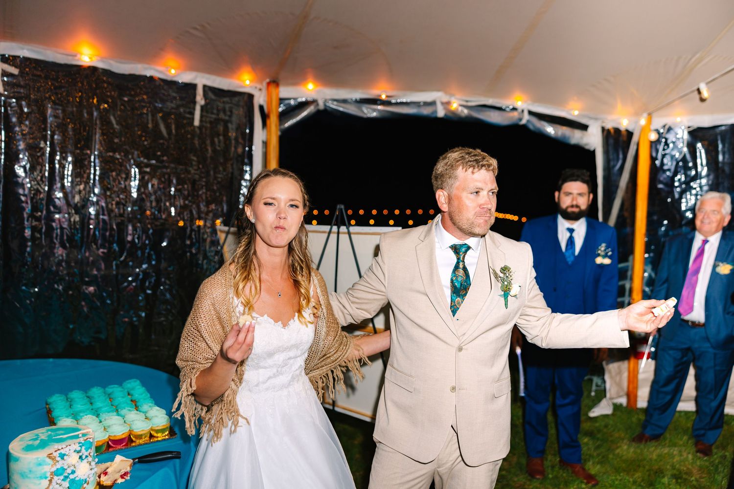 A couple celebrates at an outdoor wedding reception under a white tent as the sun sets.