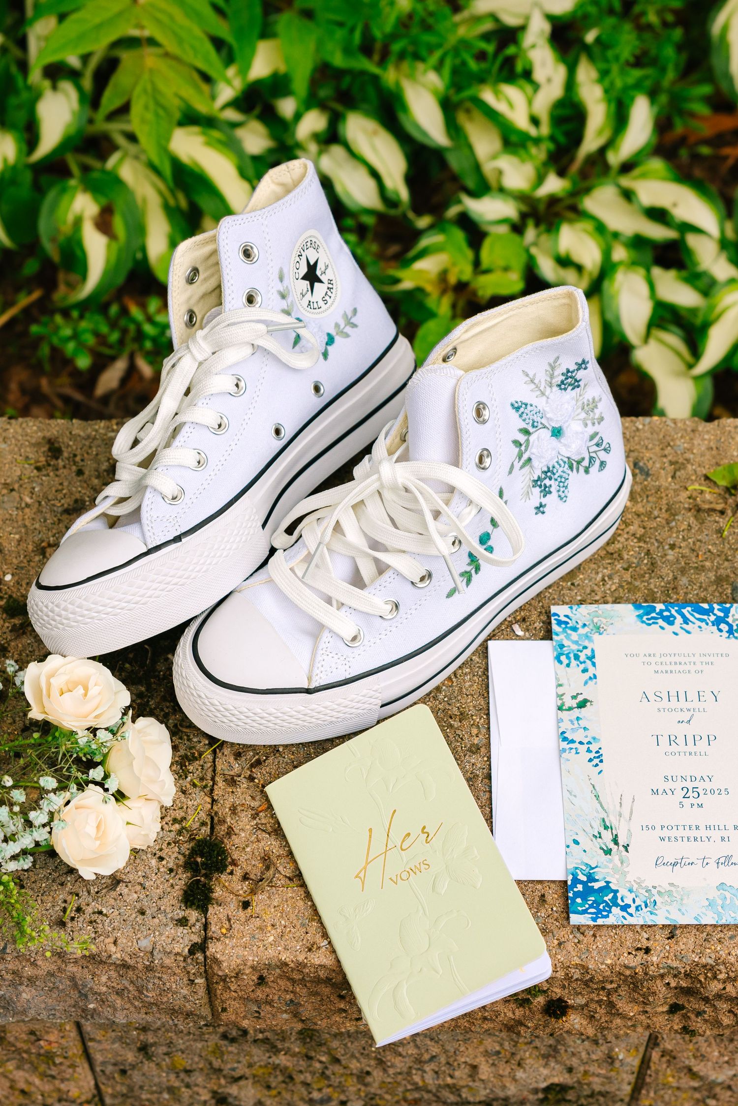White canvas sneakers with turquoise floral embroidery sit alongside wedding invitations and paper goods on a stone surface.