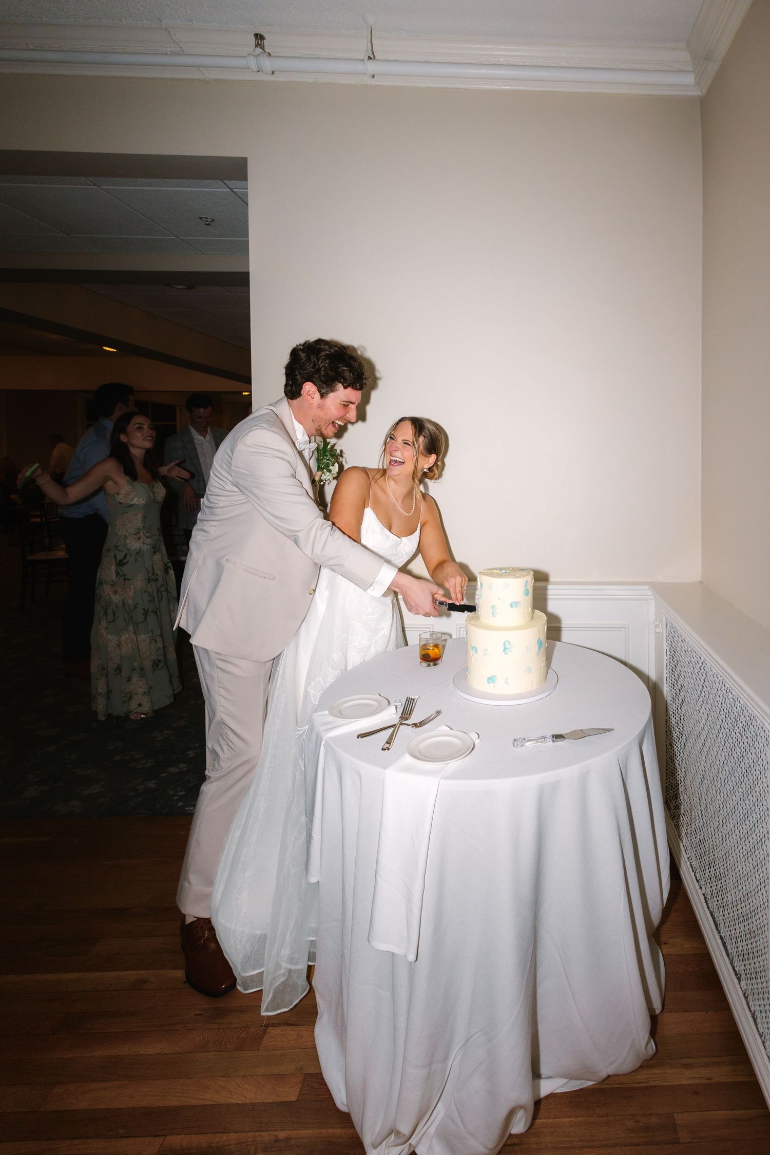 Bride and groom cutting their white tiered wedding cake together at their indoor reception at Warwick Country Club in Rhode Island.