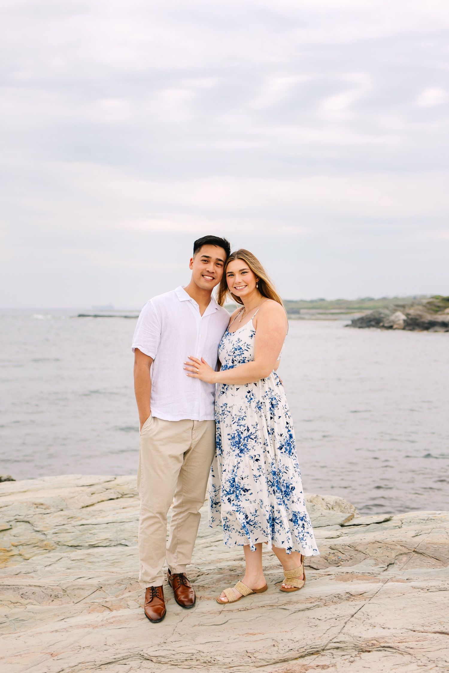 Couple posing for engagement photos on rocky coastal shore with ocean backdrop on Ocean Drive in Newport Rhode Island