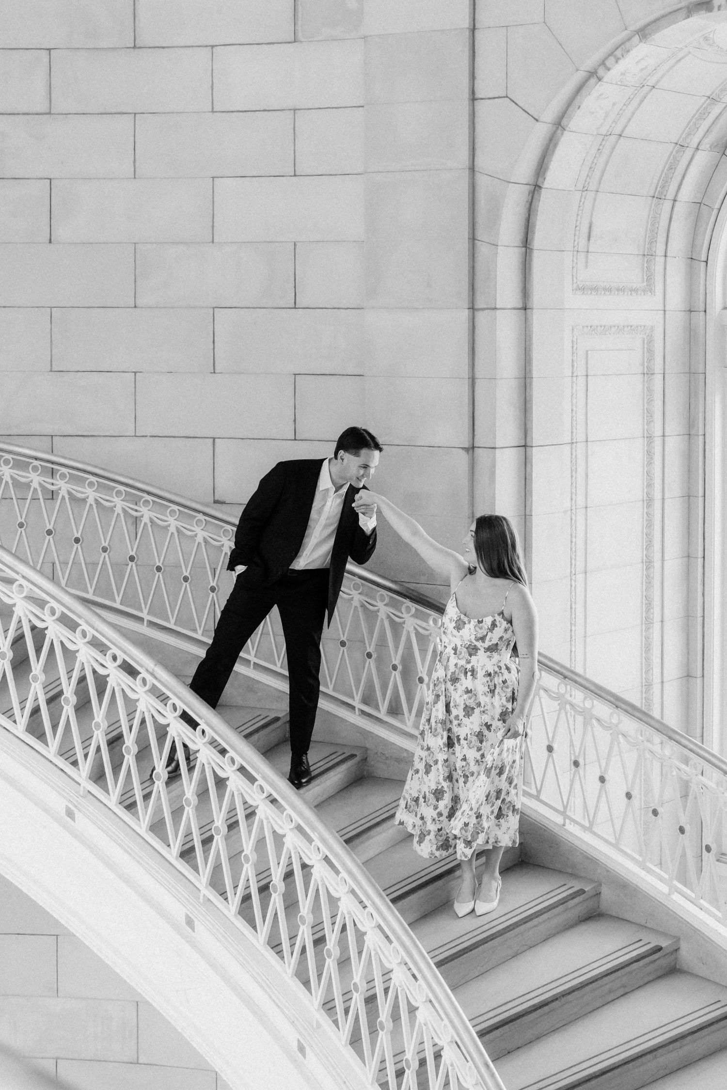 Black and white photo of man kissing womans hand on elegant staircase.