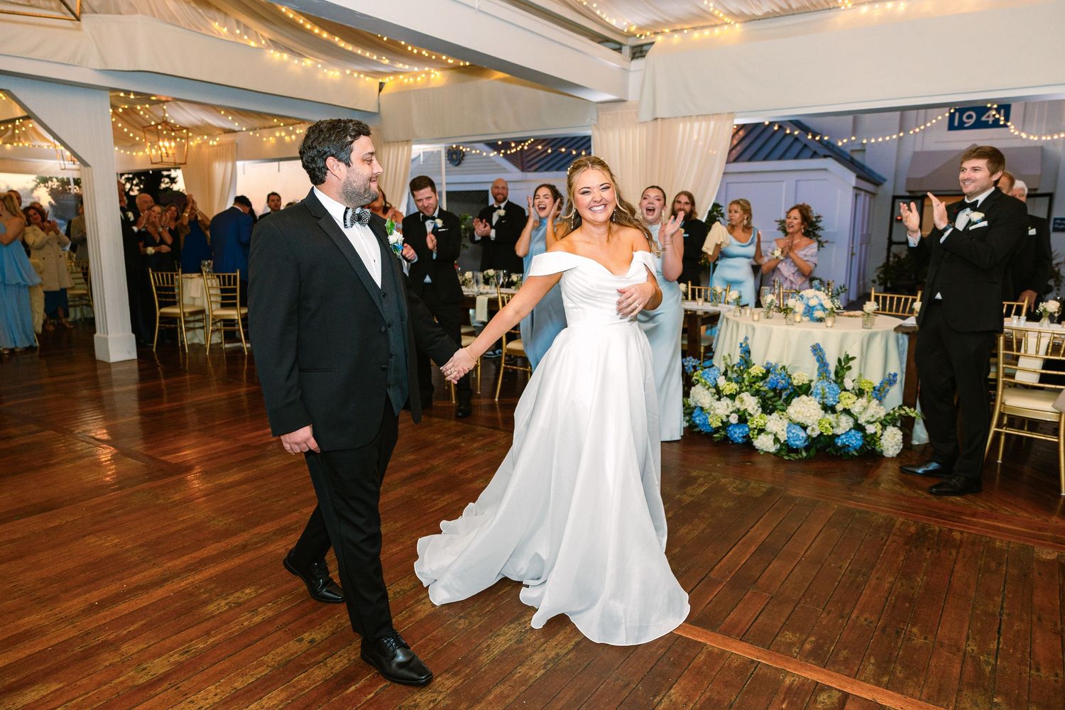 A bride and groom in formal wedding attire dances together on a wooden floor during their wedding reception at The Regatta Place in Newport