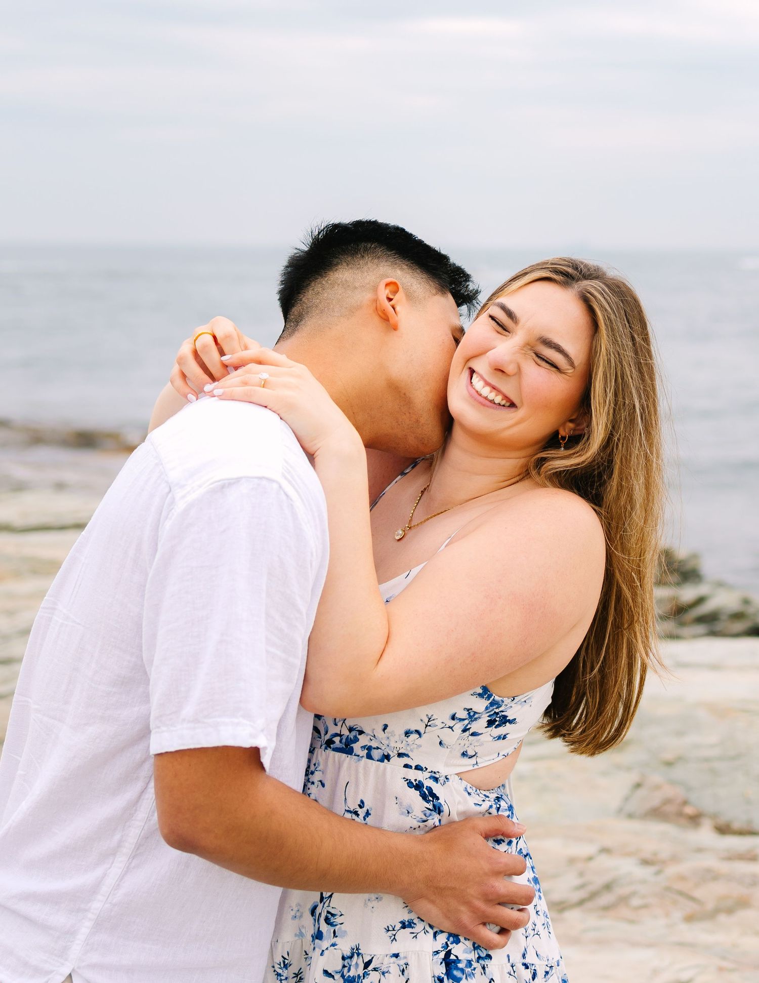 A romantic candid couples portrait after surprise proposal on Ocean Drive in Newport Rhode Island on the rocky coastal oceanside cliffs