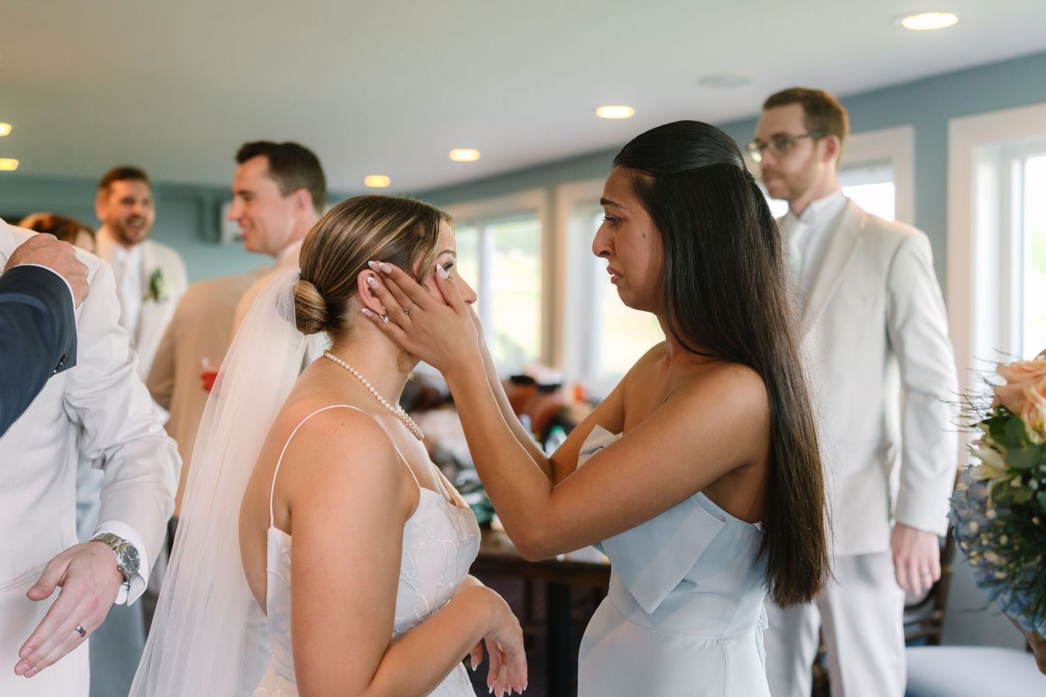 Emotional bridesmaid tenderly touches brides face in a heartfelt moment during pre-wedding preparations indoors at Warwick Country Club.