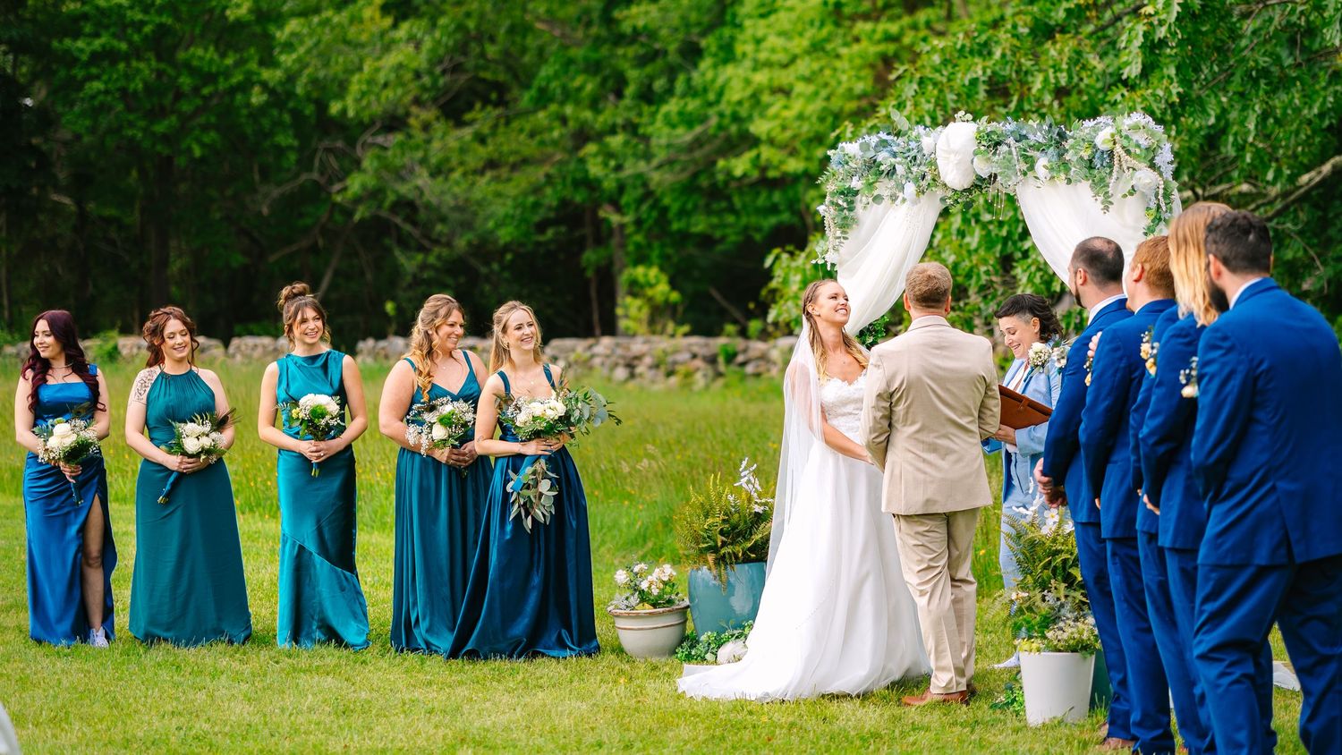 Wedding party dressed in blue and white attire enjoys a summer celebration outdoors on a lush green lawn.