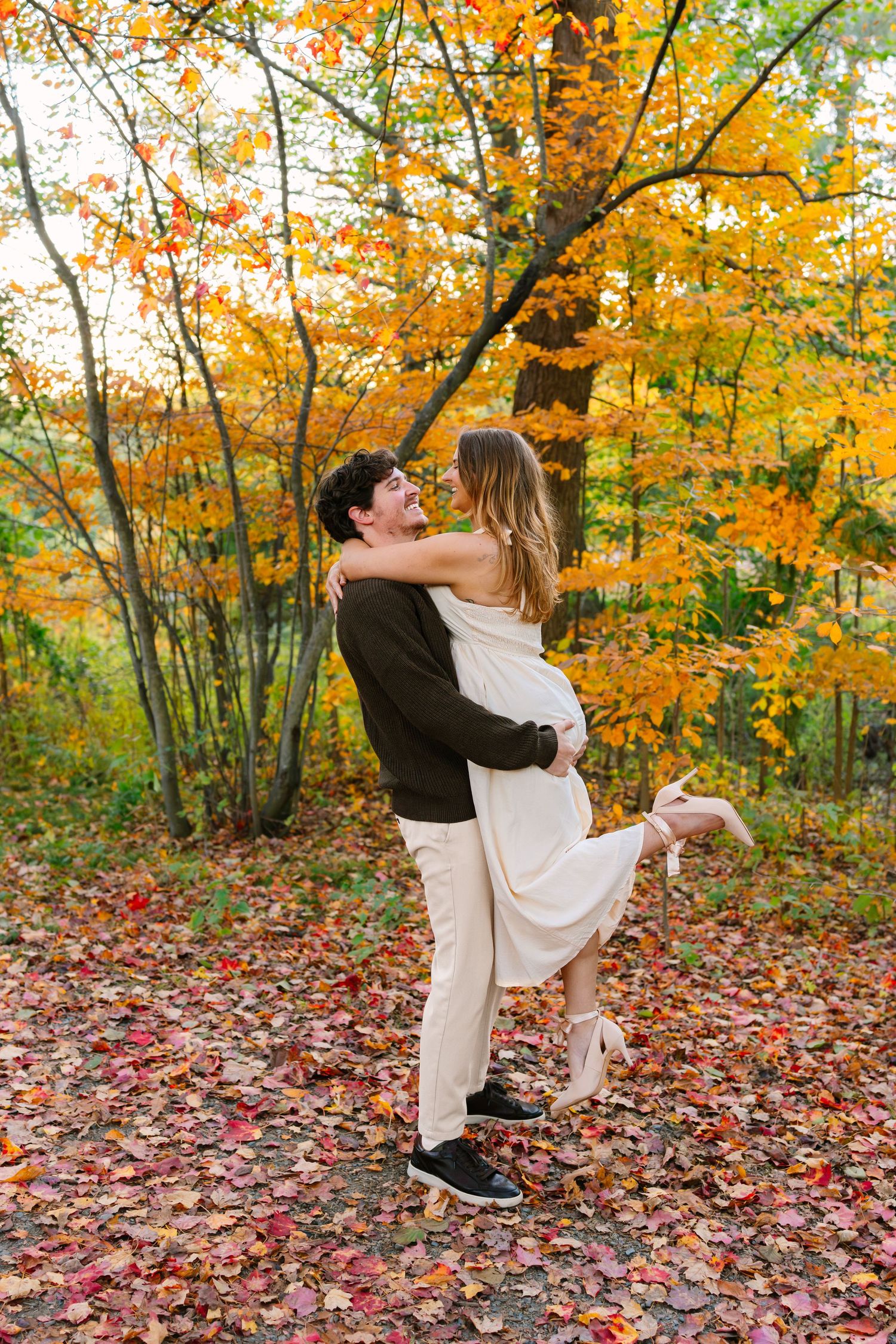 A couple dances together in a vibrant autumn forest with fallen orange and red leaves covering the ground at Arnold Arboretum in Boston MA