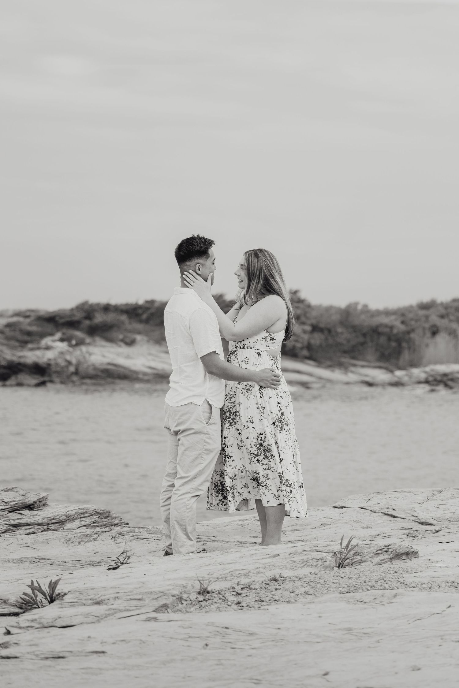 Black and white photo of a surprise proposal couple embracing on a rocky cliffside coastal area on Ocean Drive in Newport Rhode Island