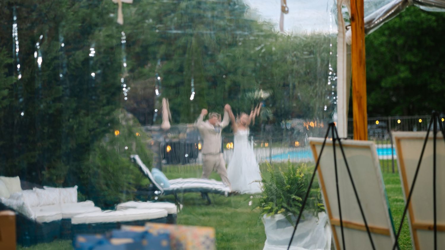 A couple in wedding attire celebrates joyfully in a backyard garden setting with swings visible in the background.