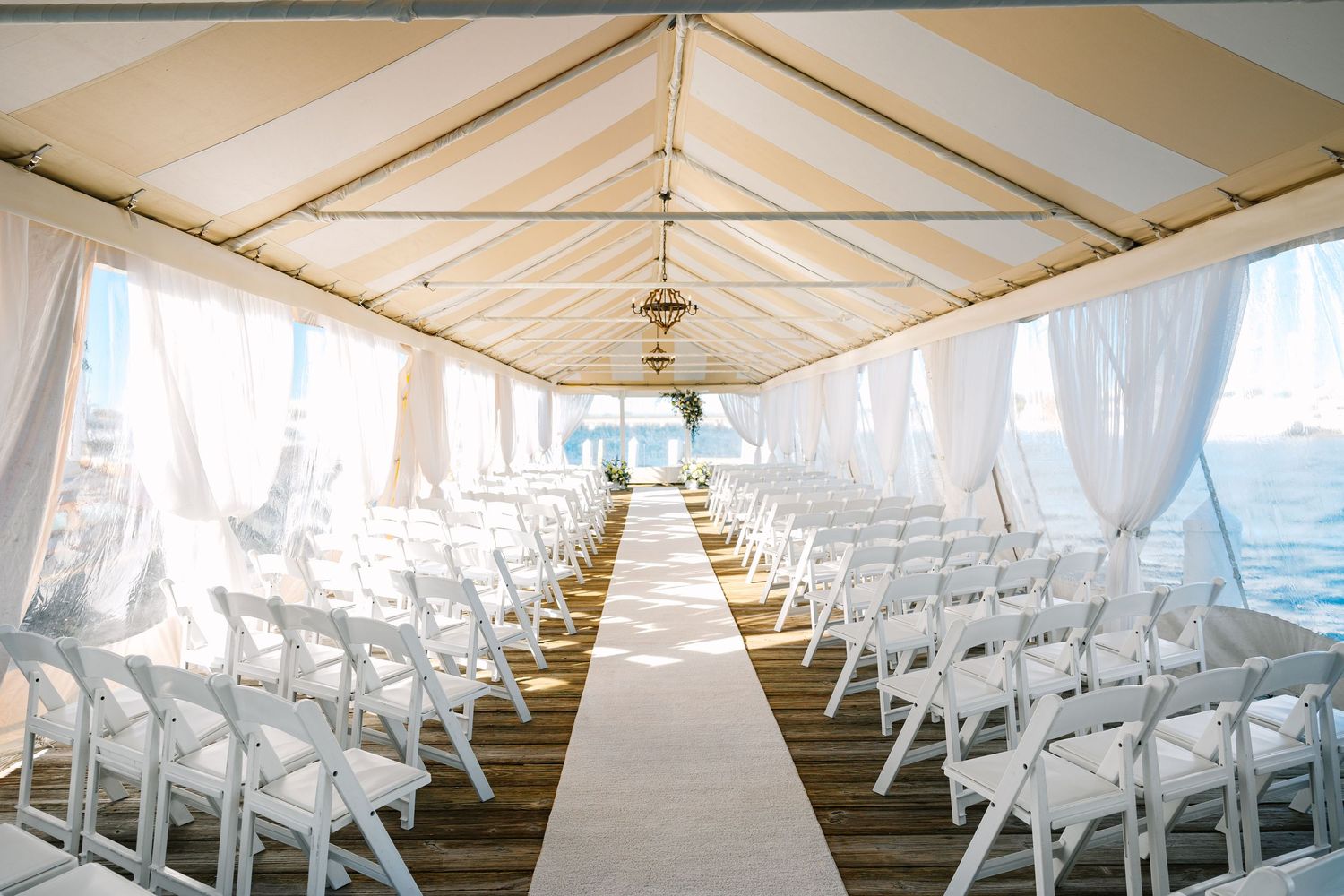 White folding chairs are arranged in neat rows under a white tent canopy for an outdoor ceremony.