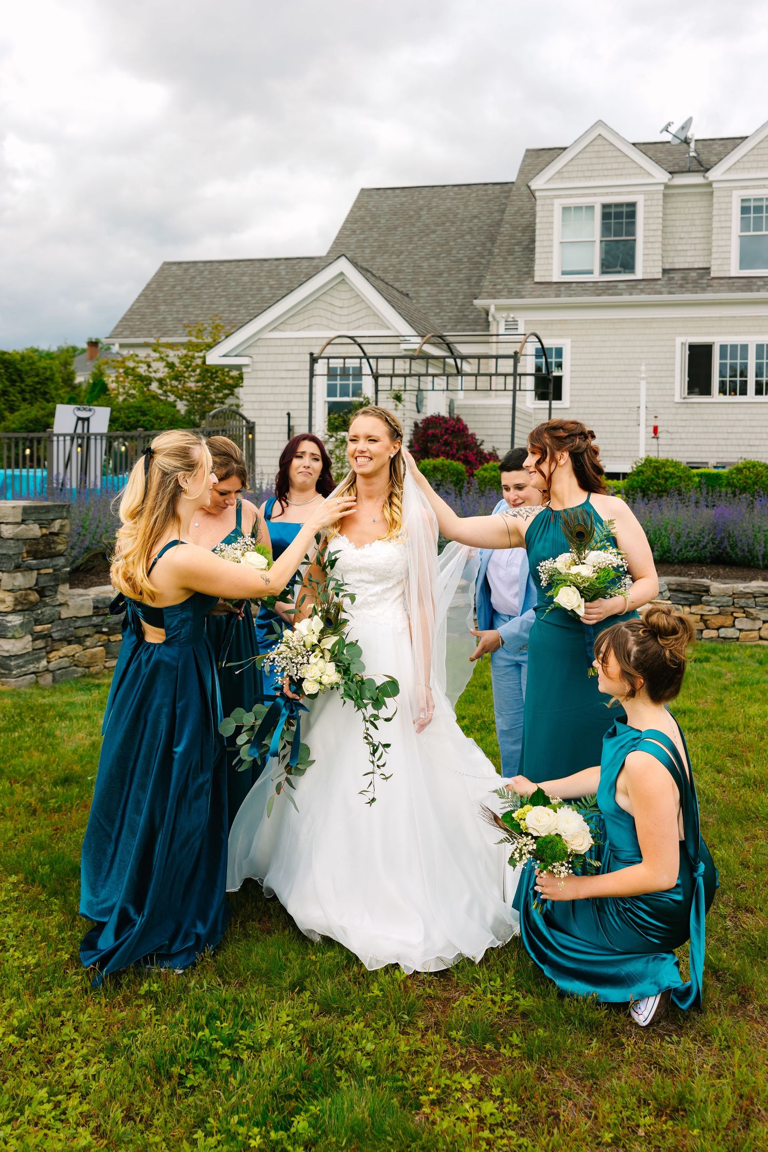 Group in teal bridesmaid dresses and white wedding gown pose together for playful outdoor wedding photos at backyard wedding in Connecticut