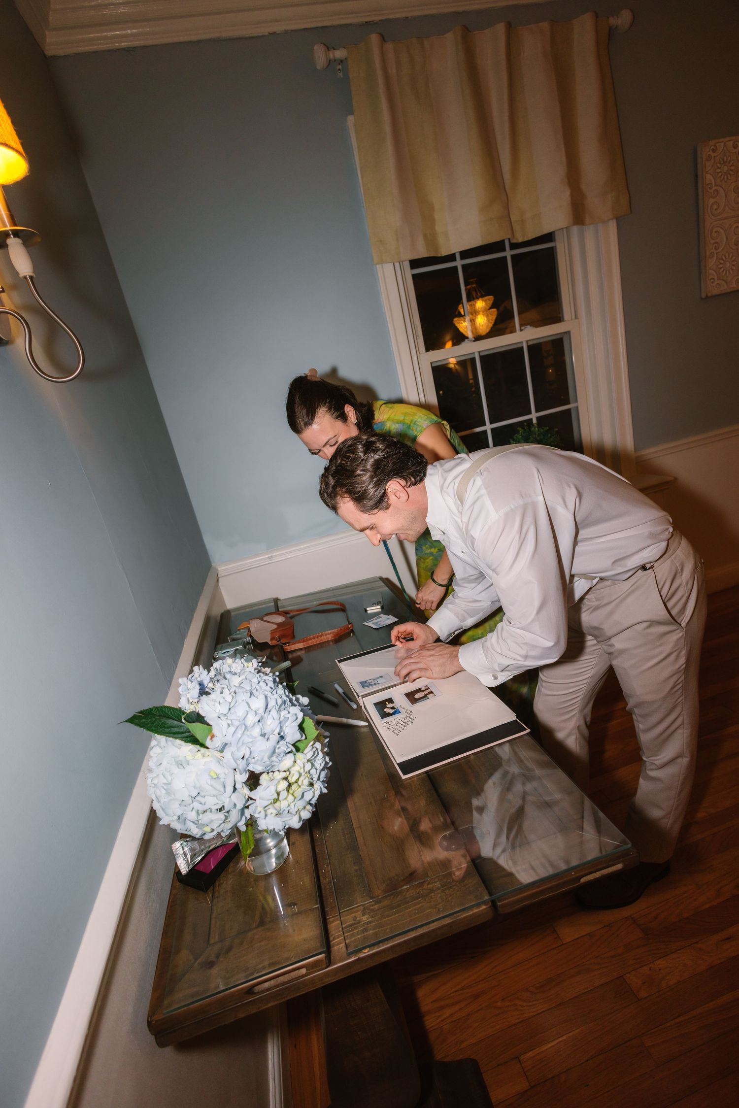 Couple signs wedding guest book at a rustic wooden table decorated with white hydrangeas.