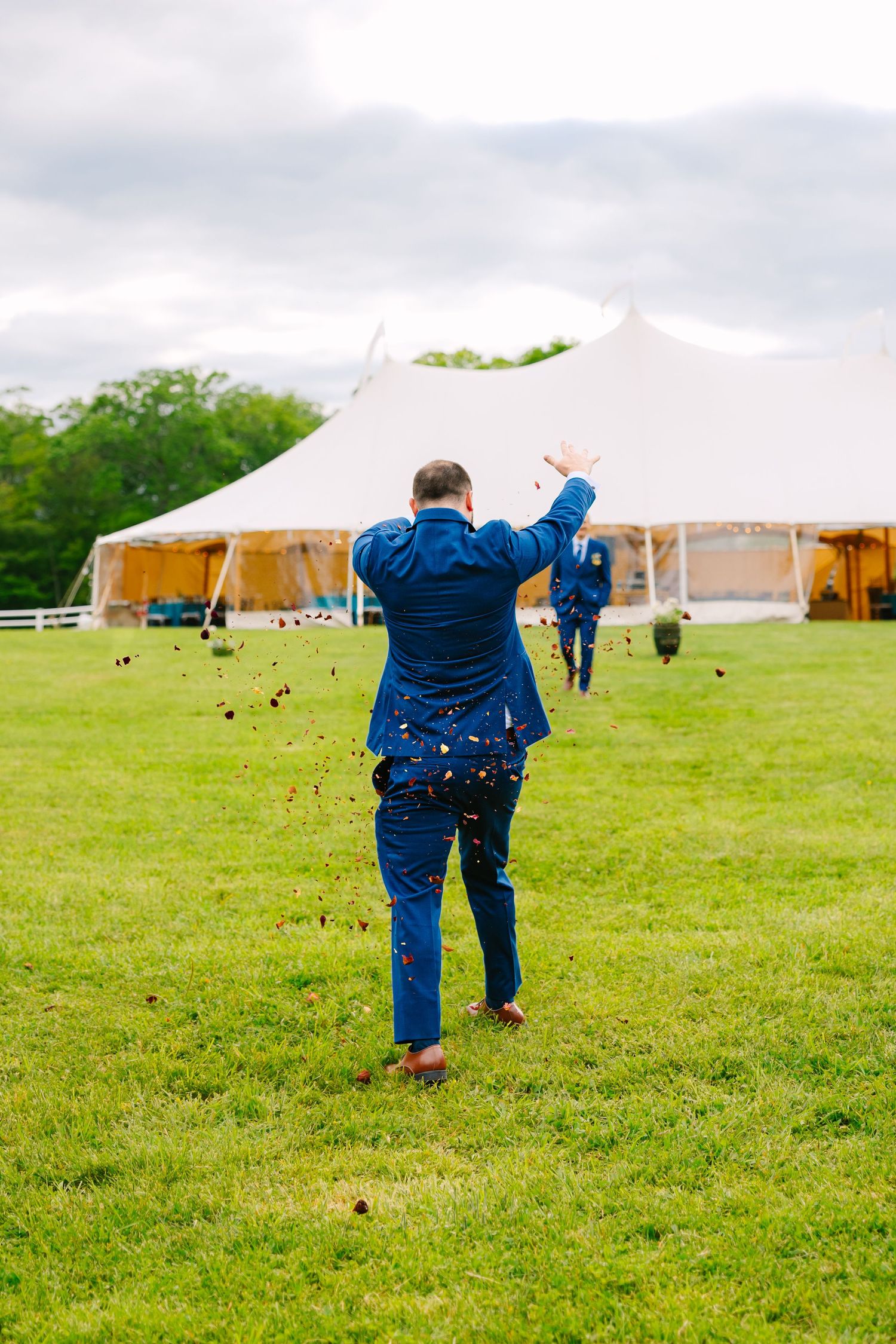 Someone in a blue suit celebrates on a green lawn with a large white tent in the background during an outdoor event.