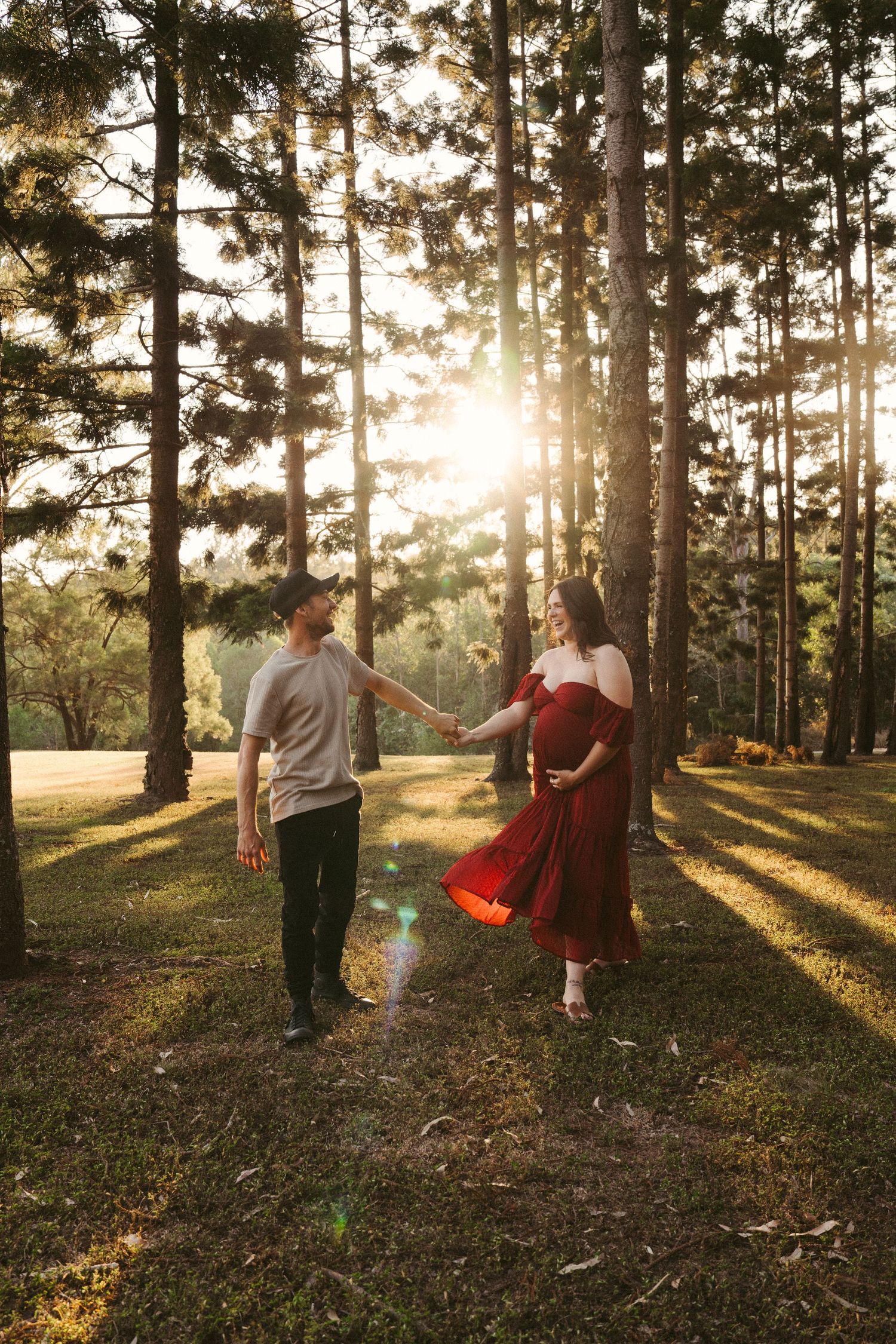 Forest maternity portrait of expectant parents holding hands among tall trees.