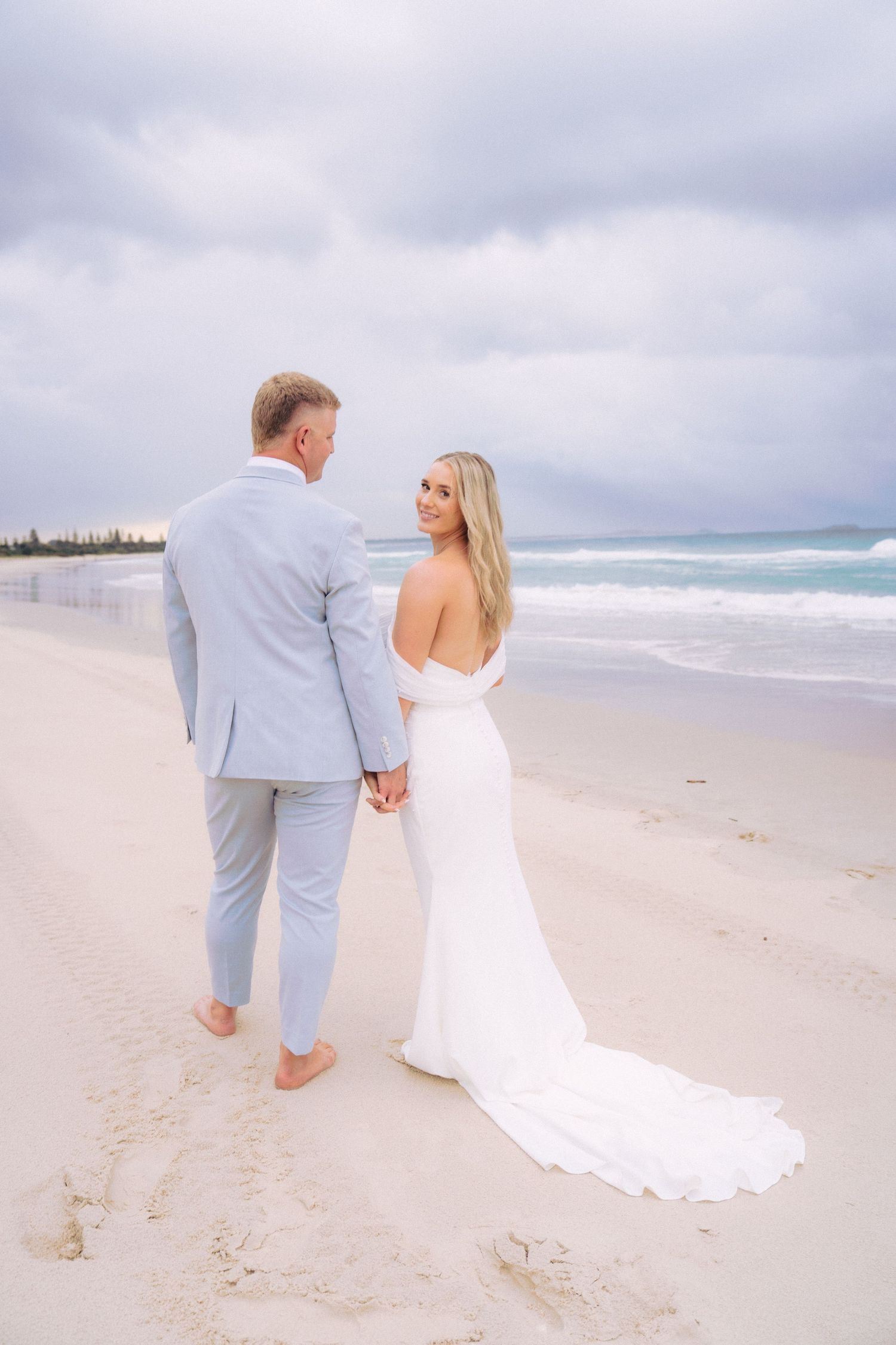 Newlyweds holding hands on the beach during their bridal portraits.