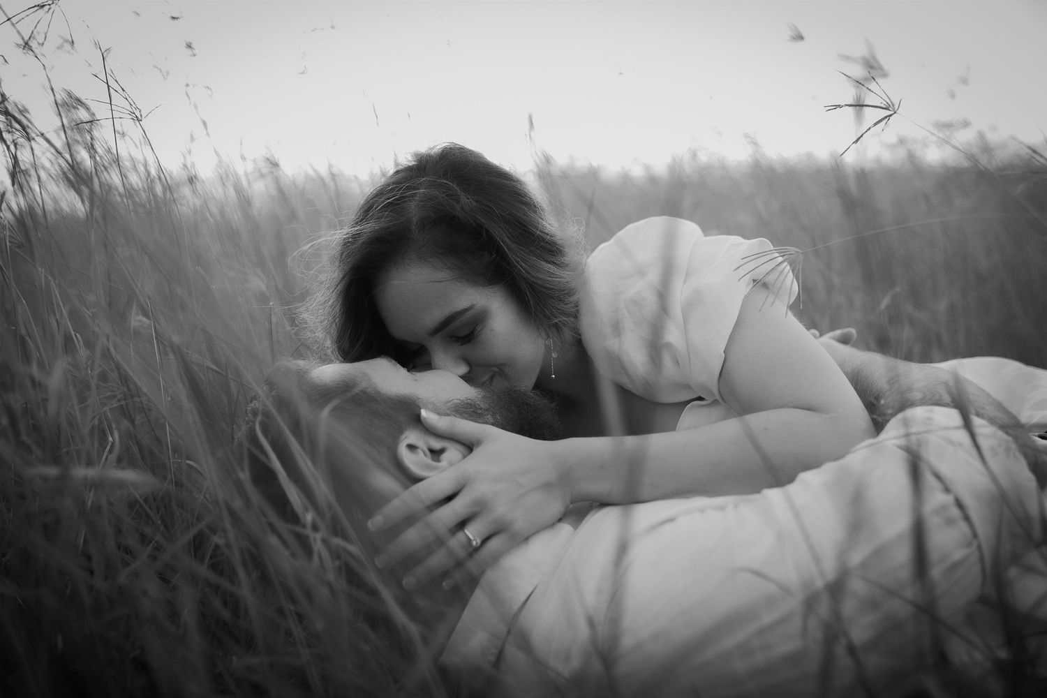 Engaged couple sharing a kiss in long grass during golden hour engagement photography.