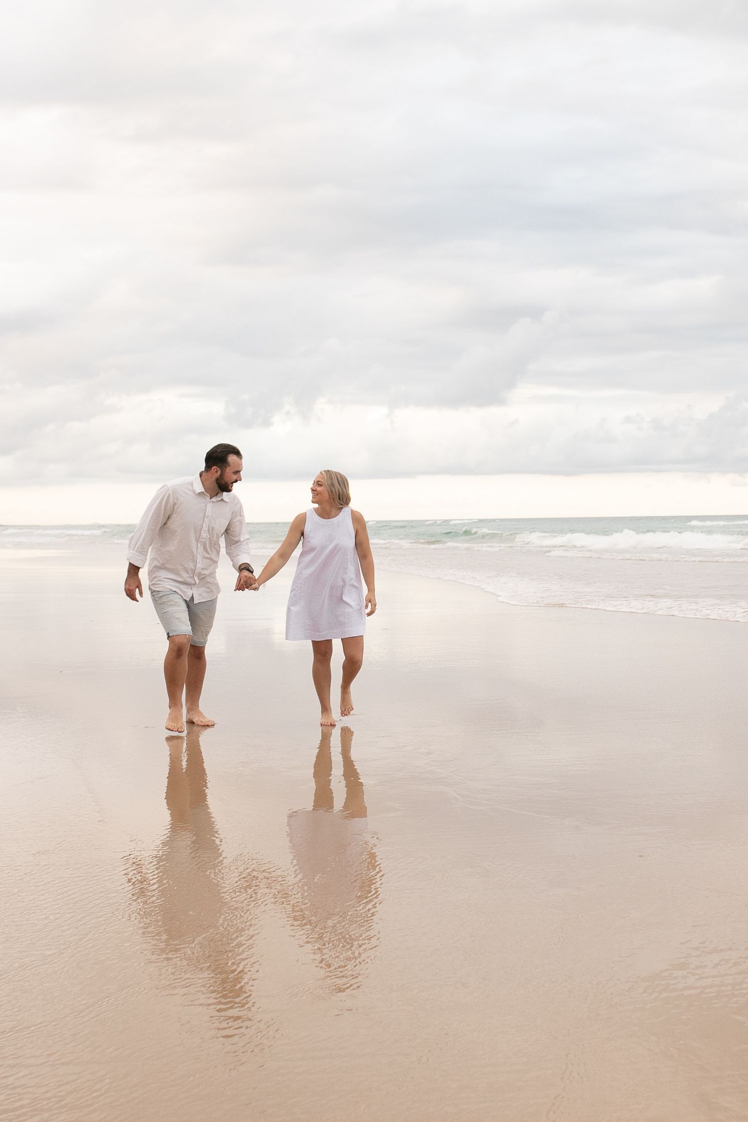 Newly engaged couple walking hand in hand along the beach during their engagement session.