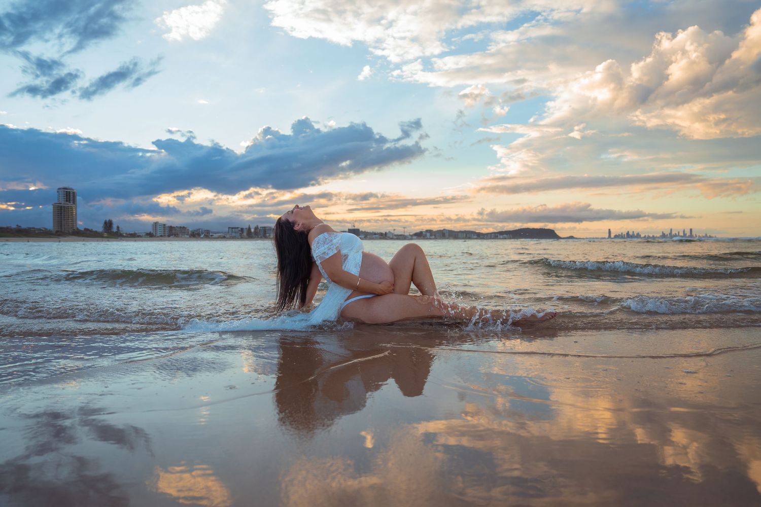 Beach maternity photography celebrating pregnancy with a golden sunset over the coastline.